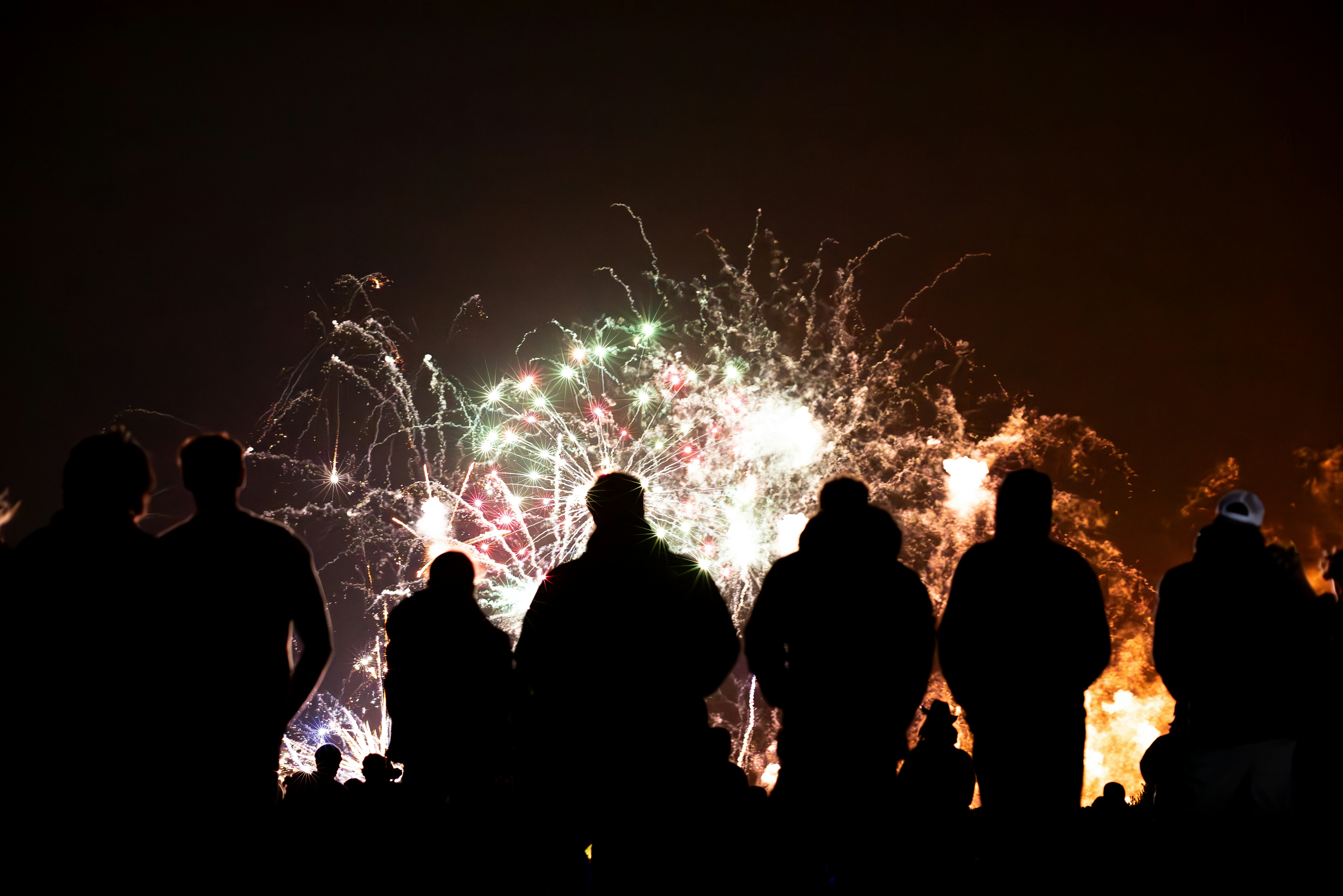 Silhouettes of people watching fireworks display at night.