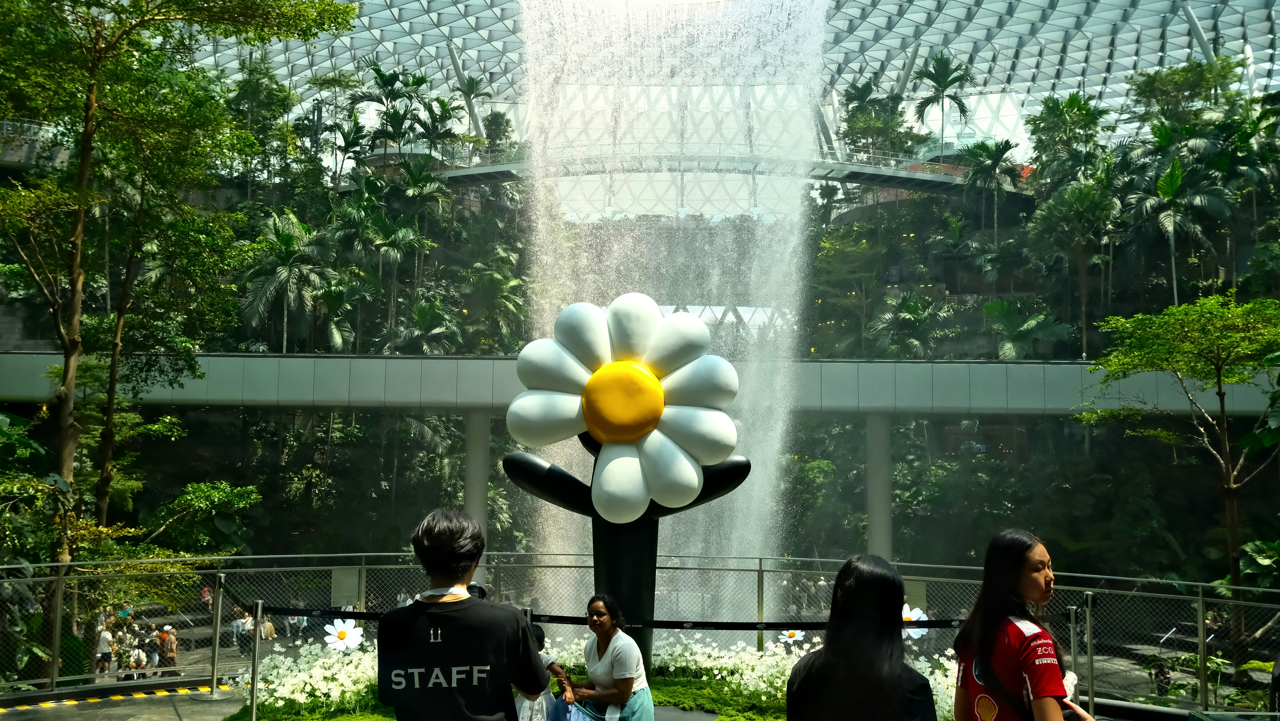 Giant flower sculpture with waterfall in lush indoor garden.