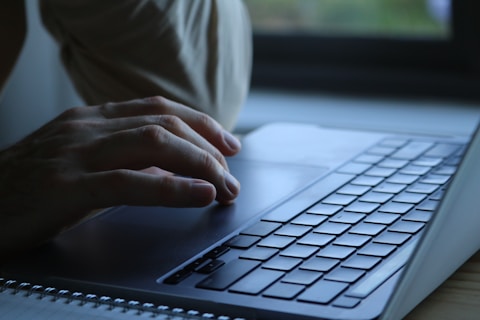 Person typing on a laptop keyboard by window