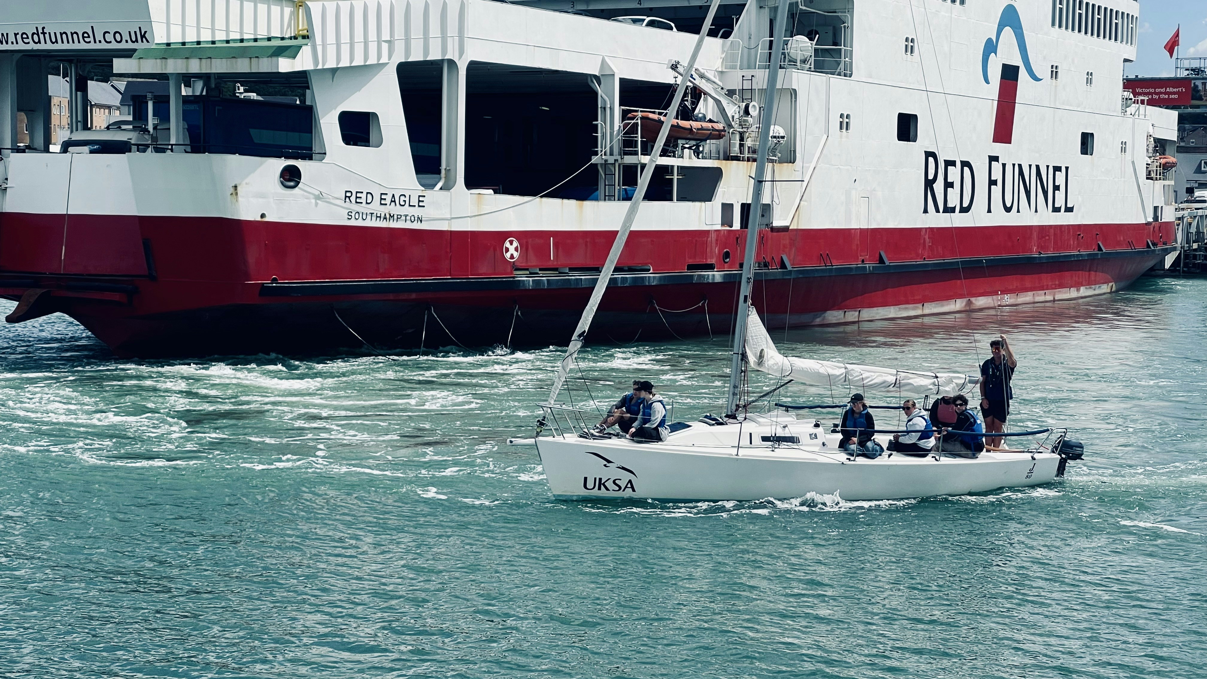 大きな赤い漏斗フェリーの近くを航行するヨット。