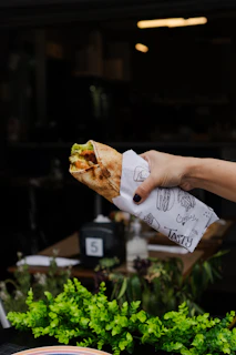 Hand holding a wrapped food item with decorative paper.