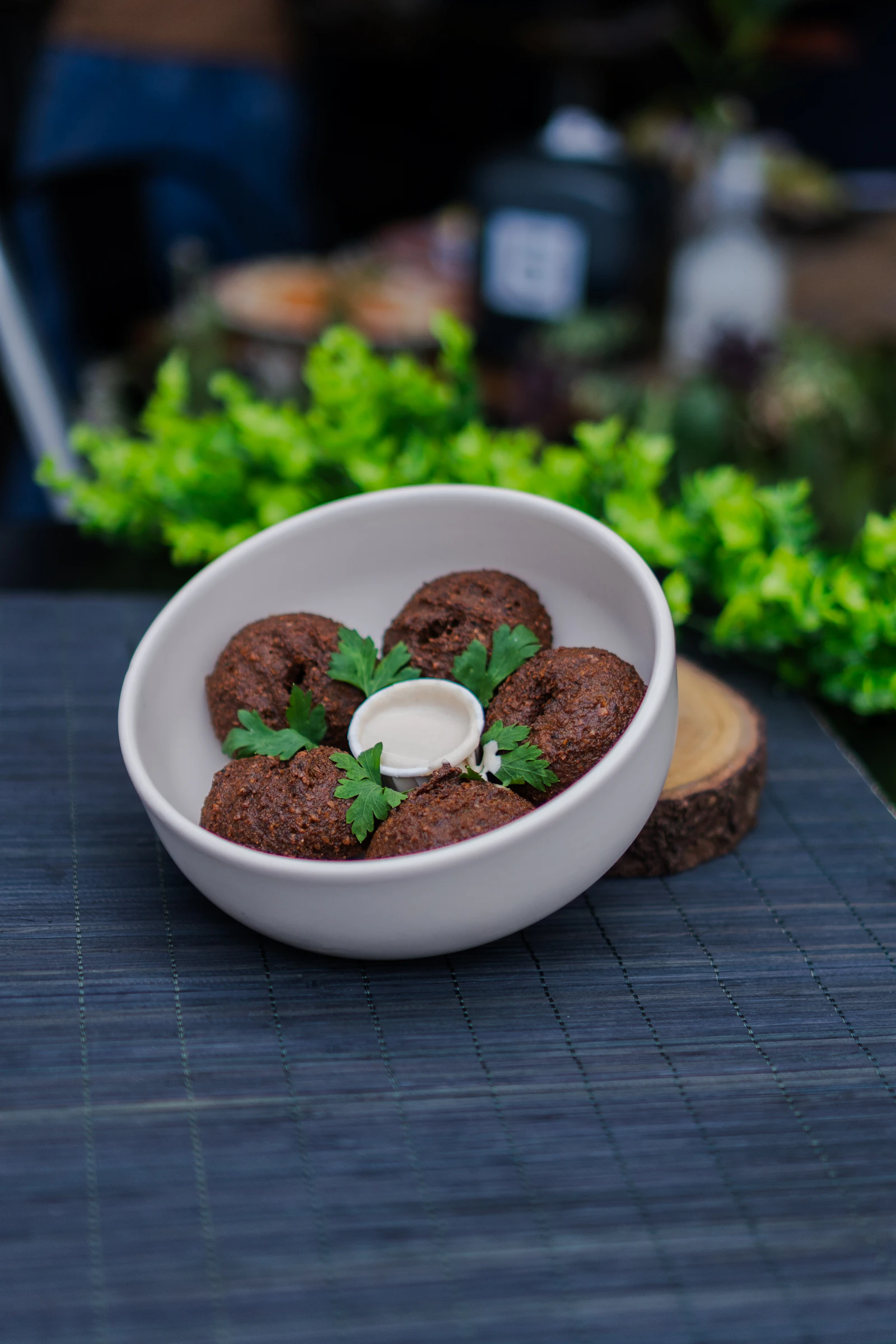 Illustrative image for vegan food in cairo: ful, taameya and koshari: Five fried falafel beside a pale dipping sauce and parsley in a dark bowl.