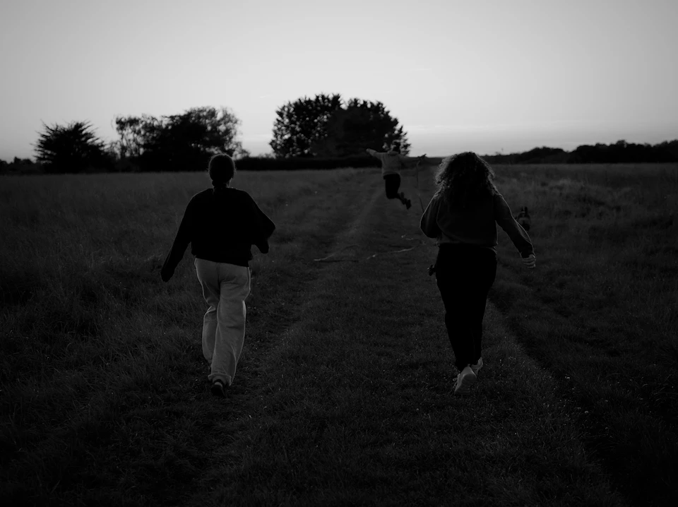 Group of people walking on dirt path through grassy field with trees in background
