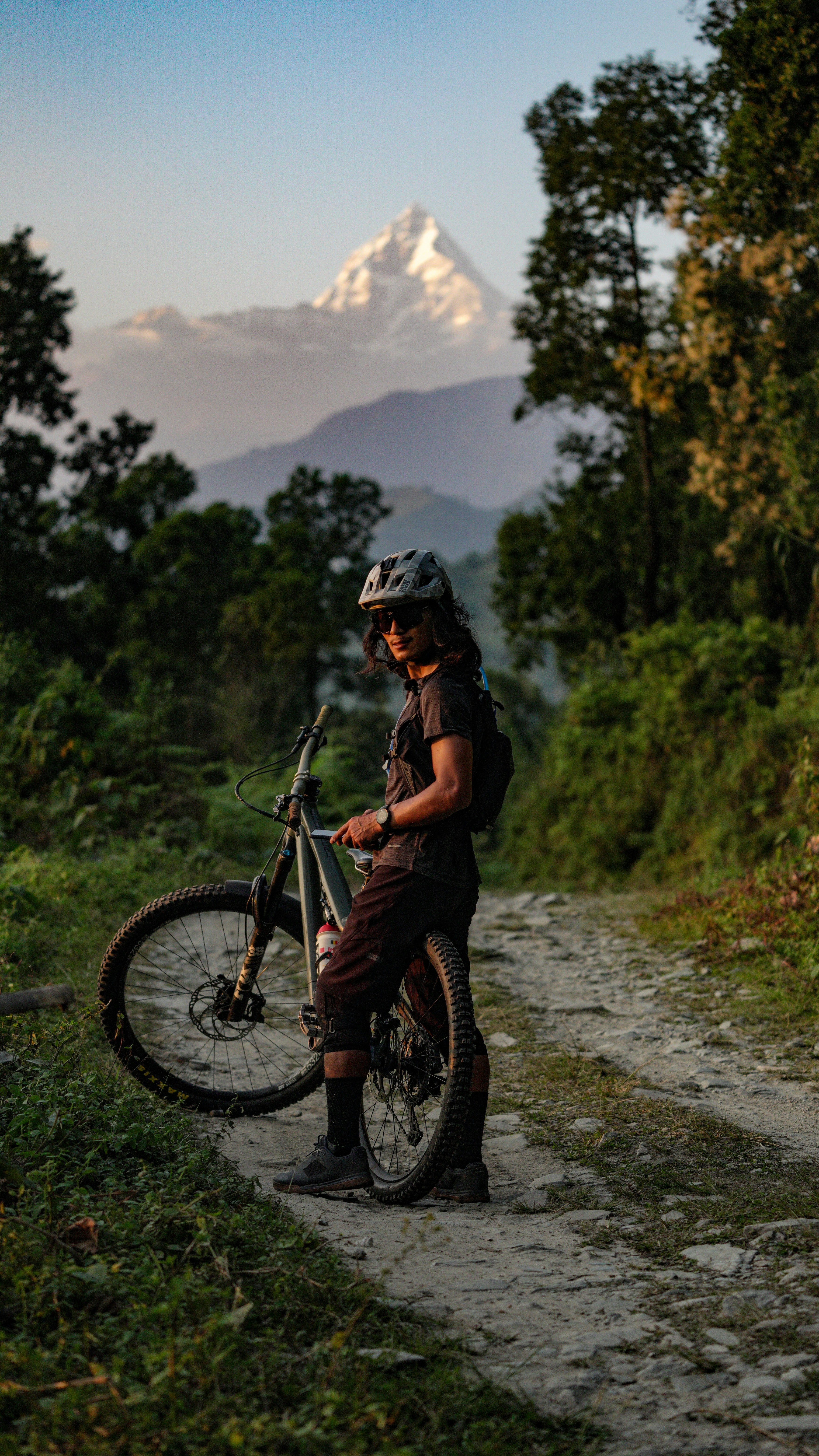 Mountain biker with bicycle on dirt road at sunset.