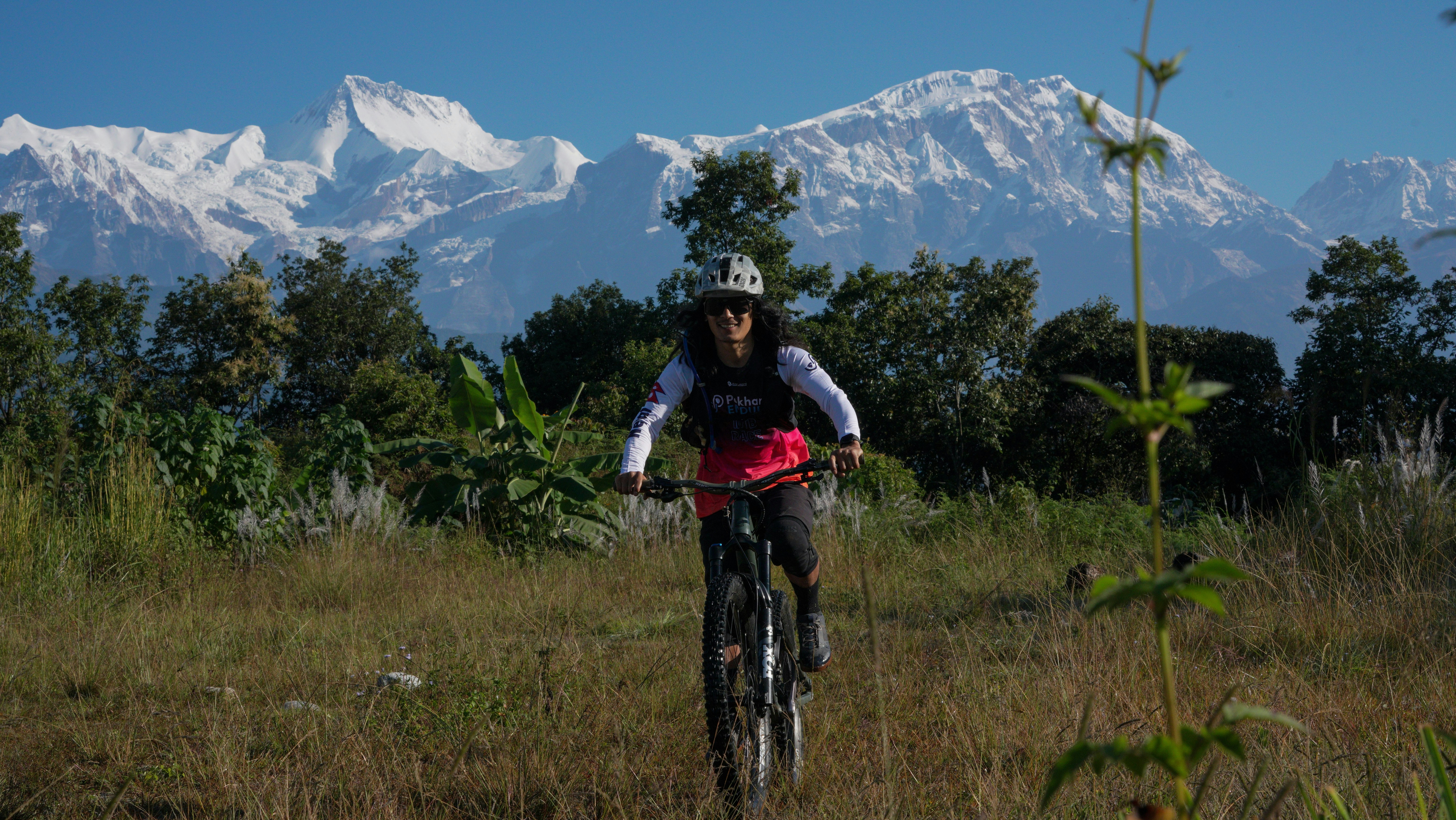 Woman mountain biking with snowy peaks behind.