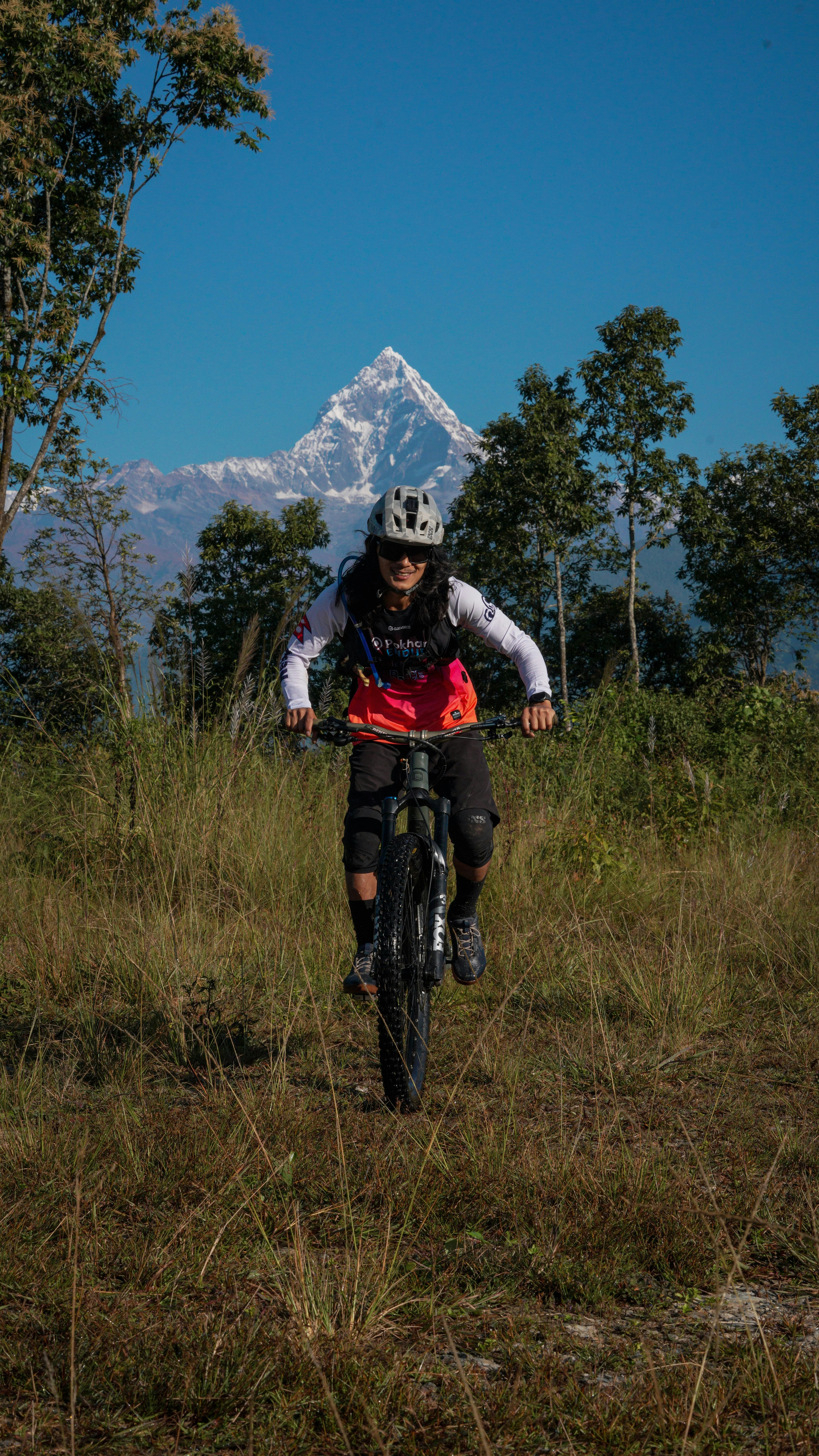 Mountain biker rides through grassy field with snowy peak behind