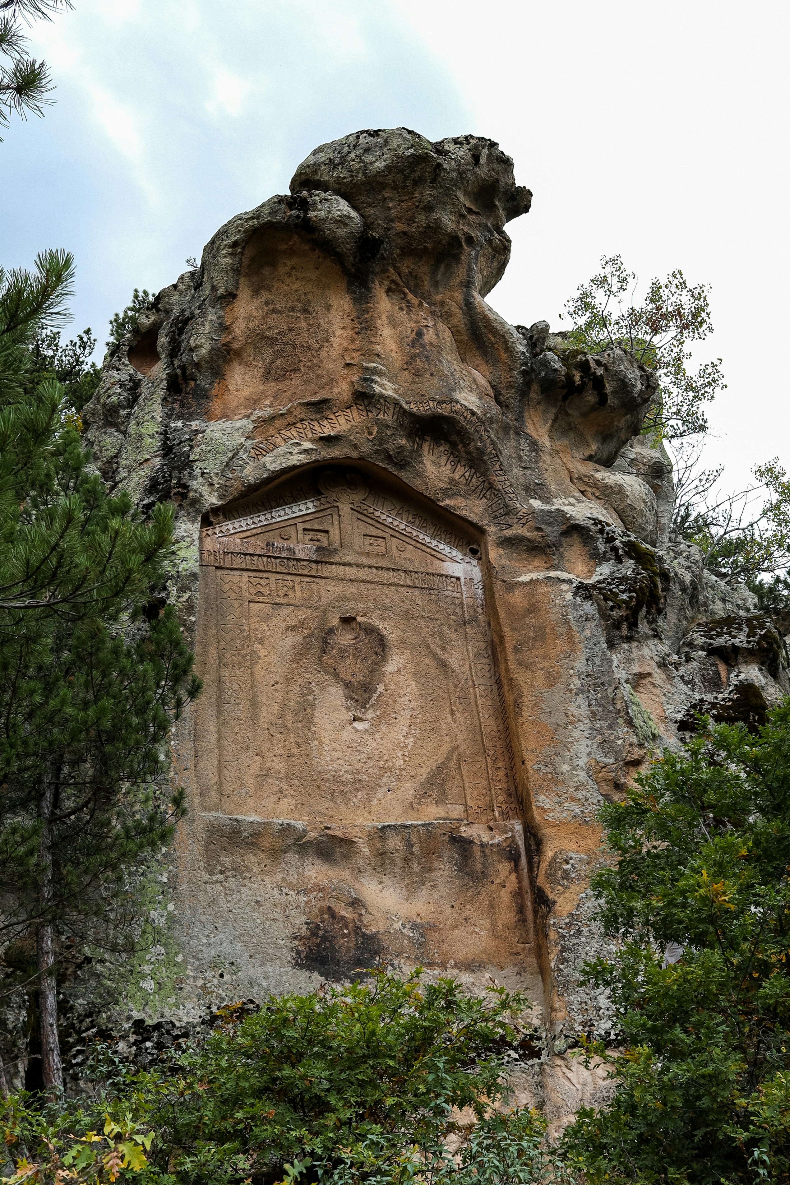 Uralte Felszeichnungen in einer bewaldeten Berglandschaft.