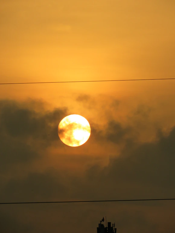 Bright sun partially obscured by clouds at sunset