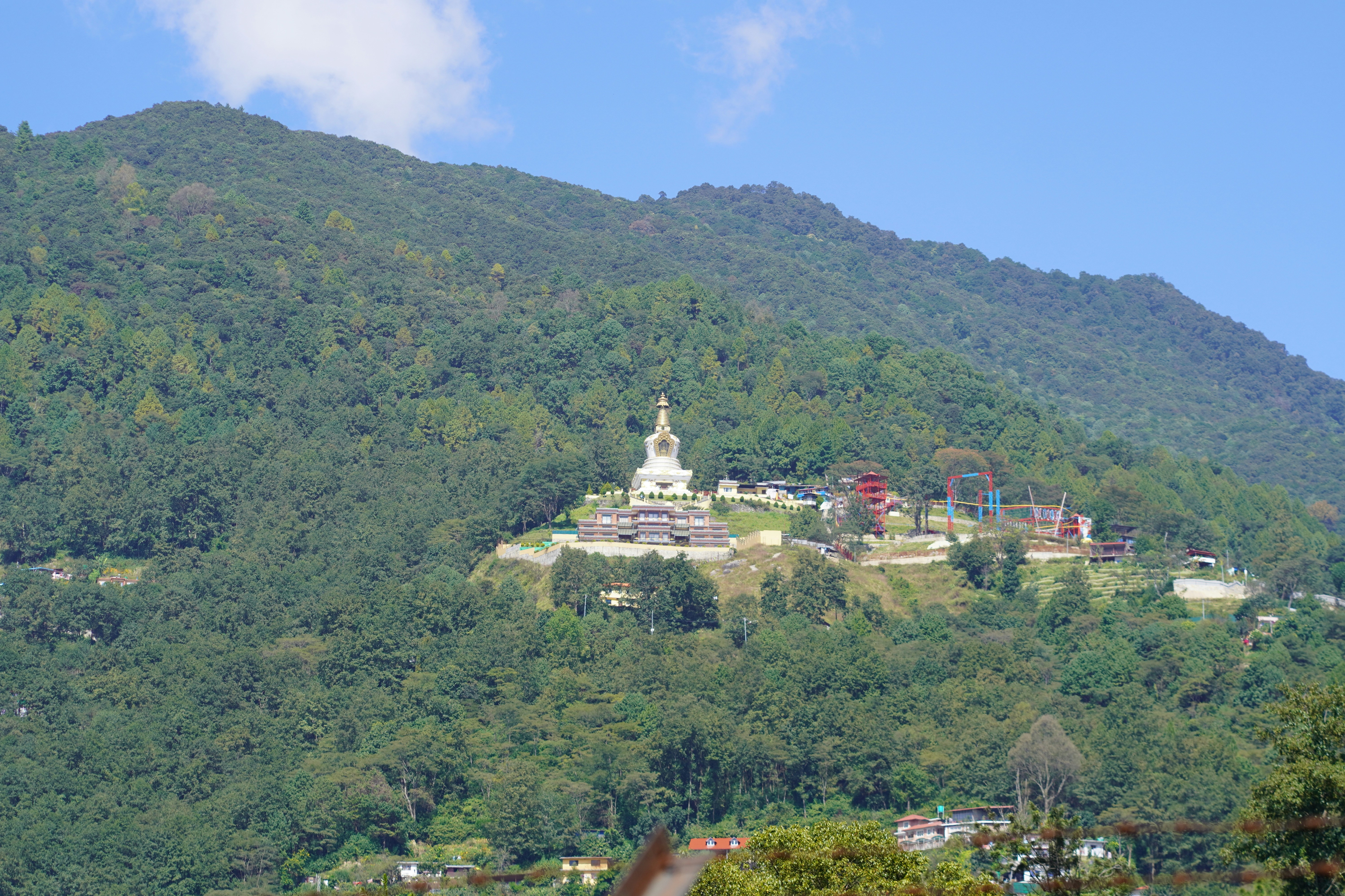 A white stupa sits on a forested mountain slope.