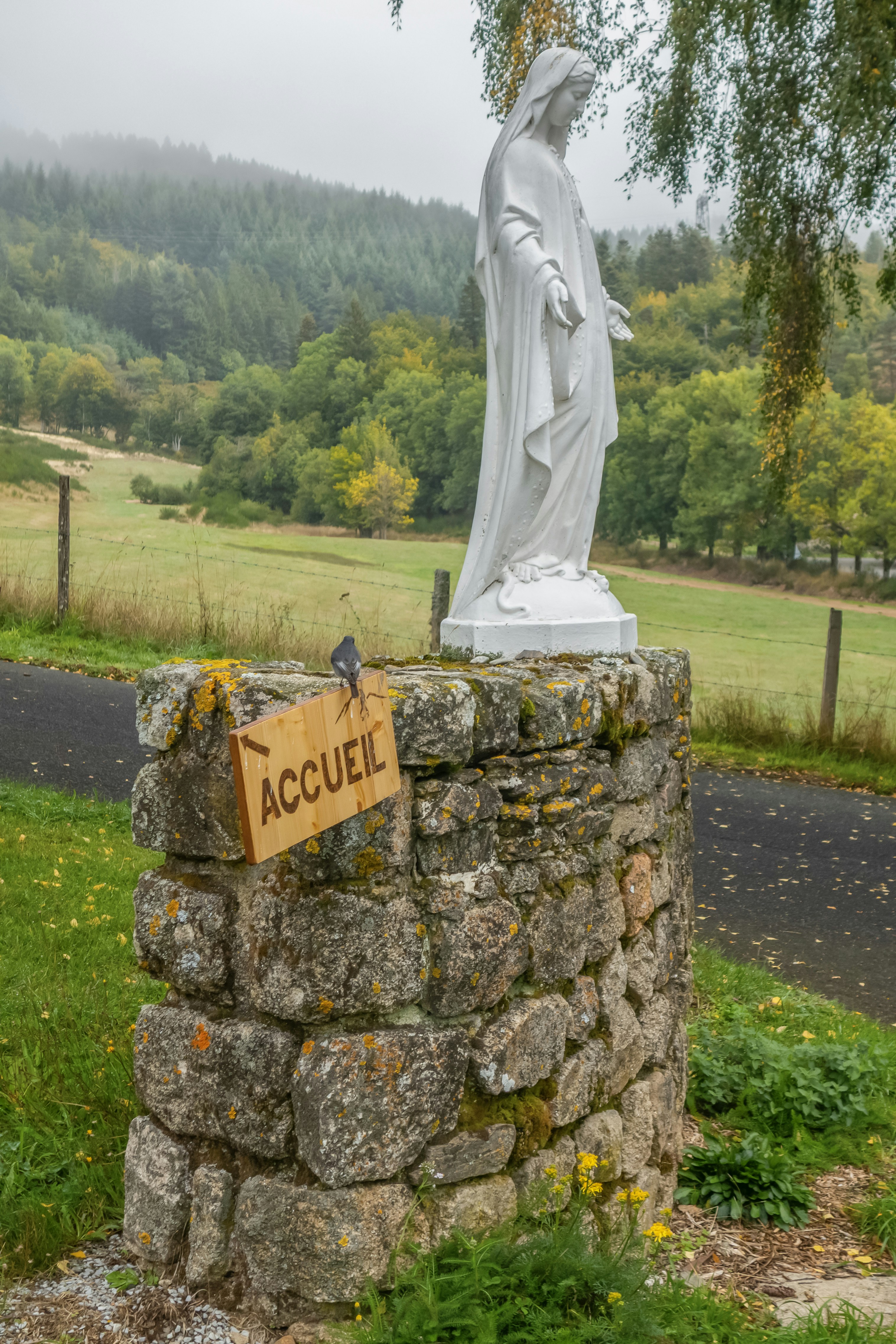 White statue of mary on stone pedestal with welcome sign.
