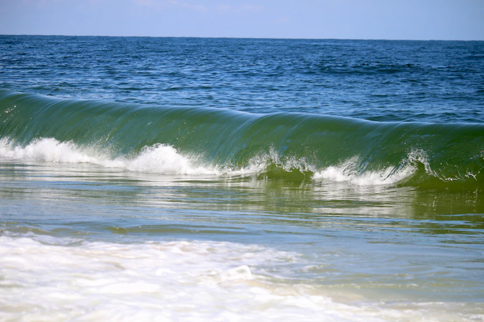 Large curling wave crashes onto the shore in a vibrant green color against blue water