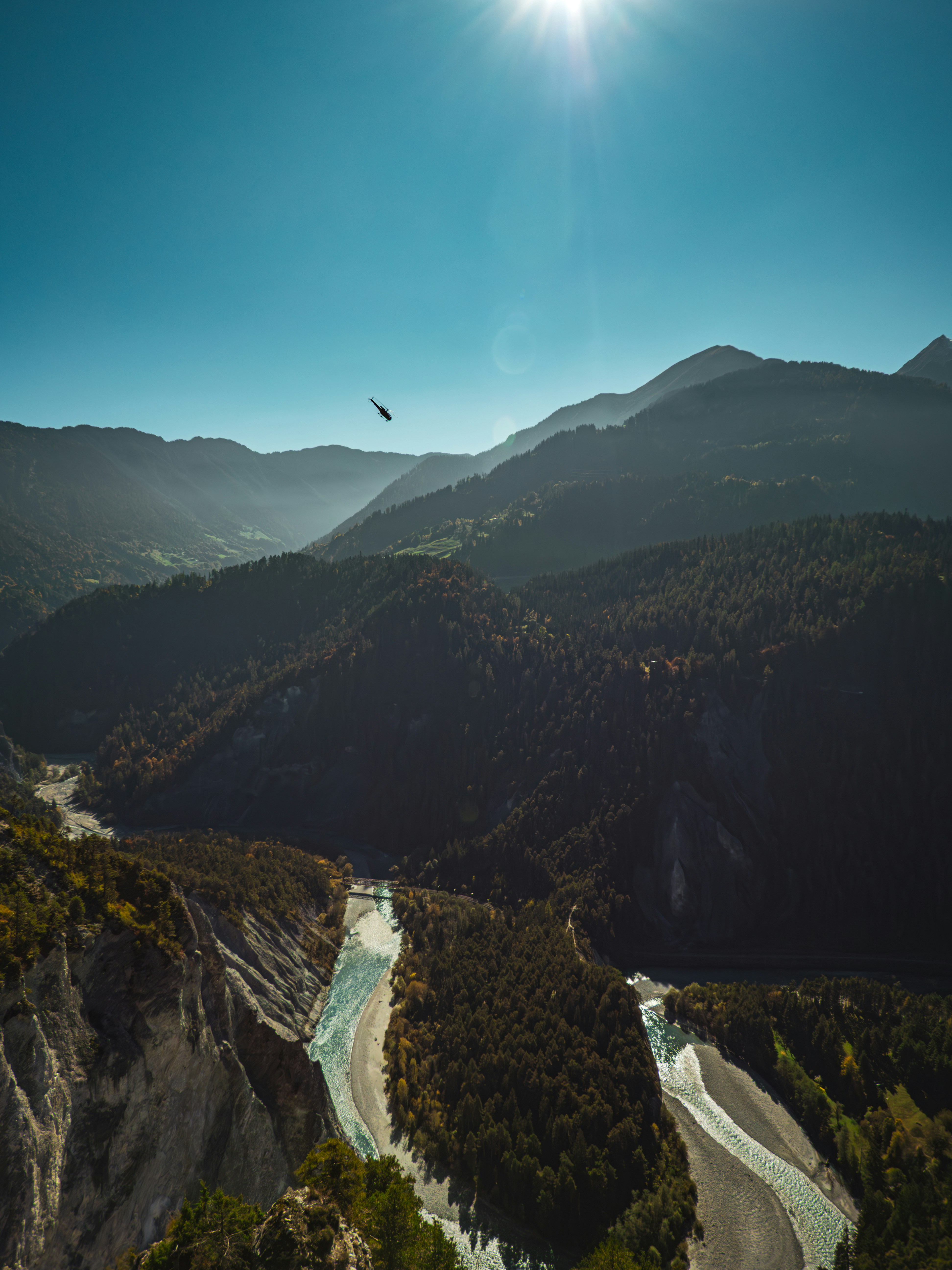 Sun shines over a winding river in a mountain valley.