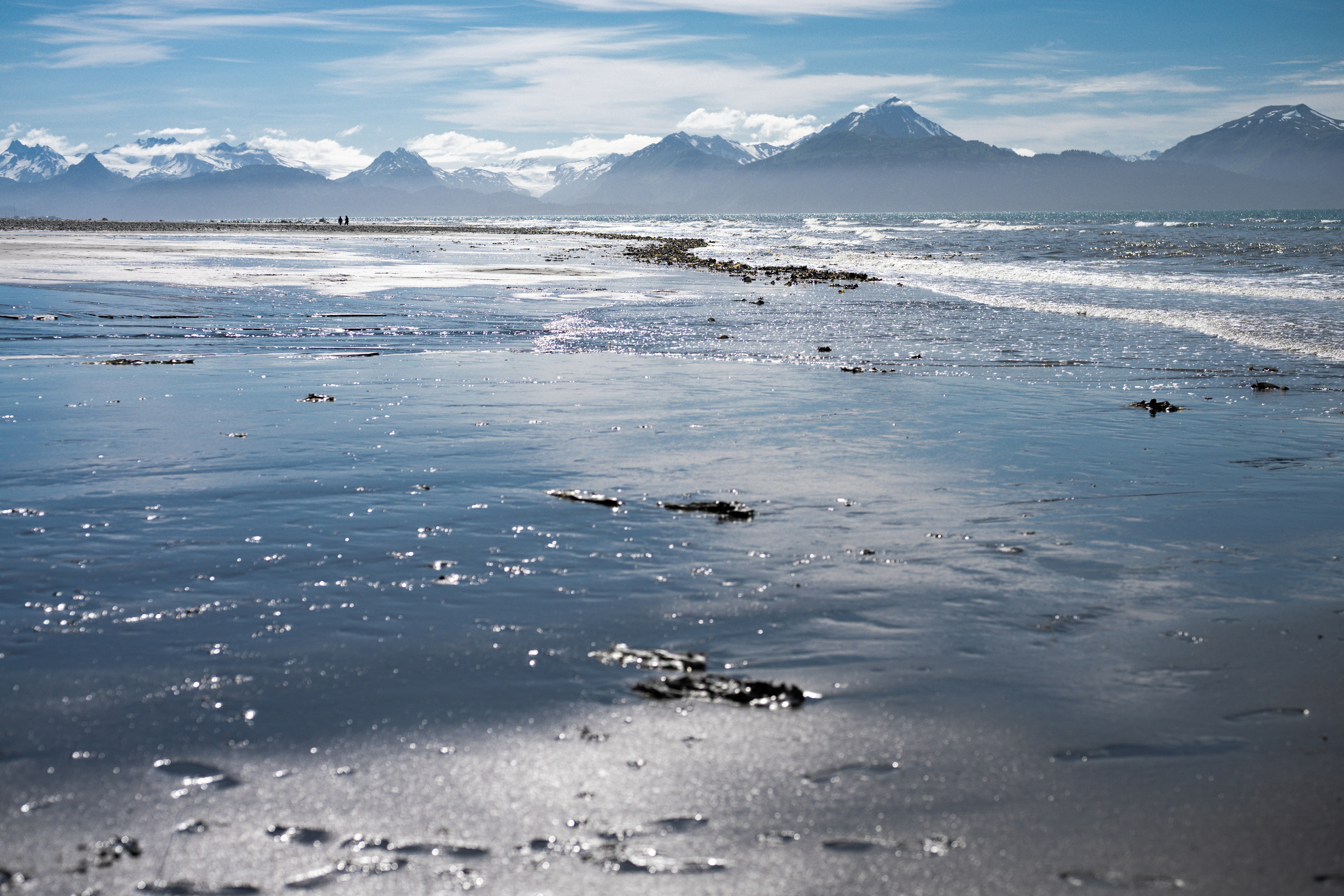 Wet sandy beach with distant snow-capped mountains.