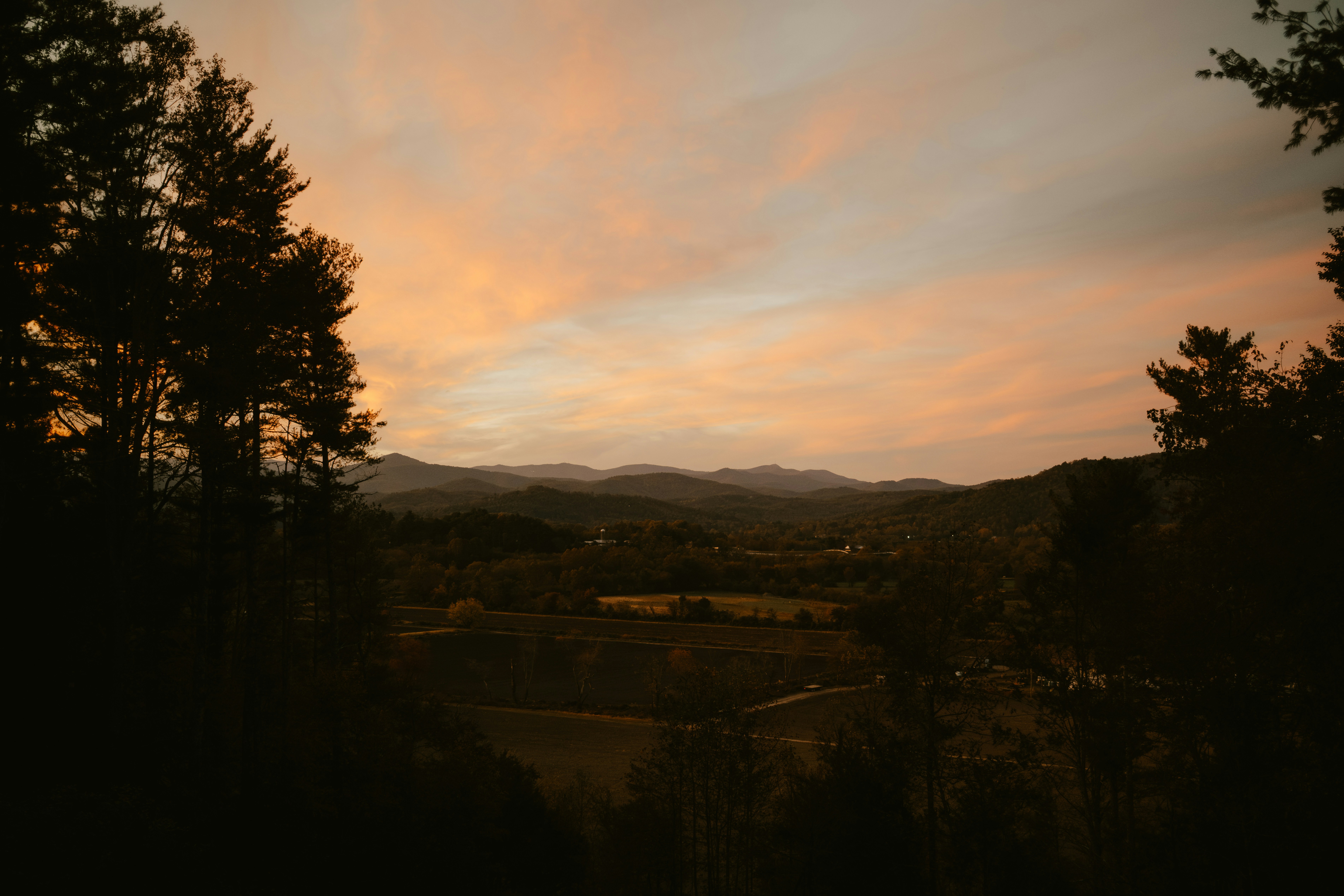 Hills and trees under a colorful sunset sky.