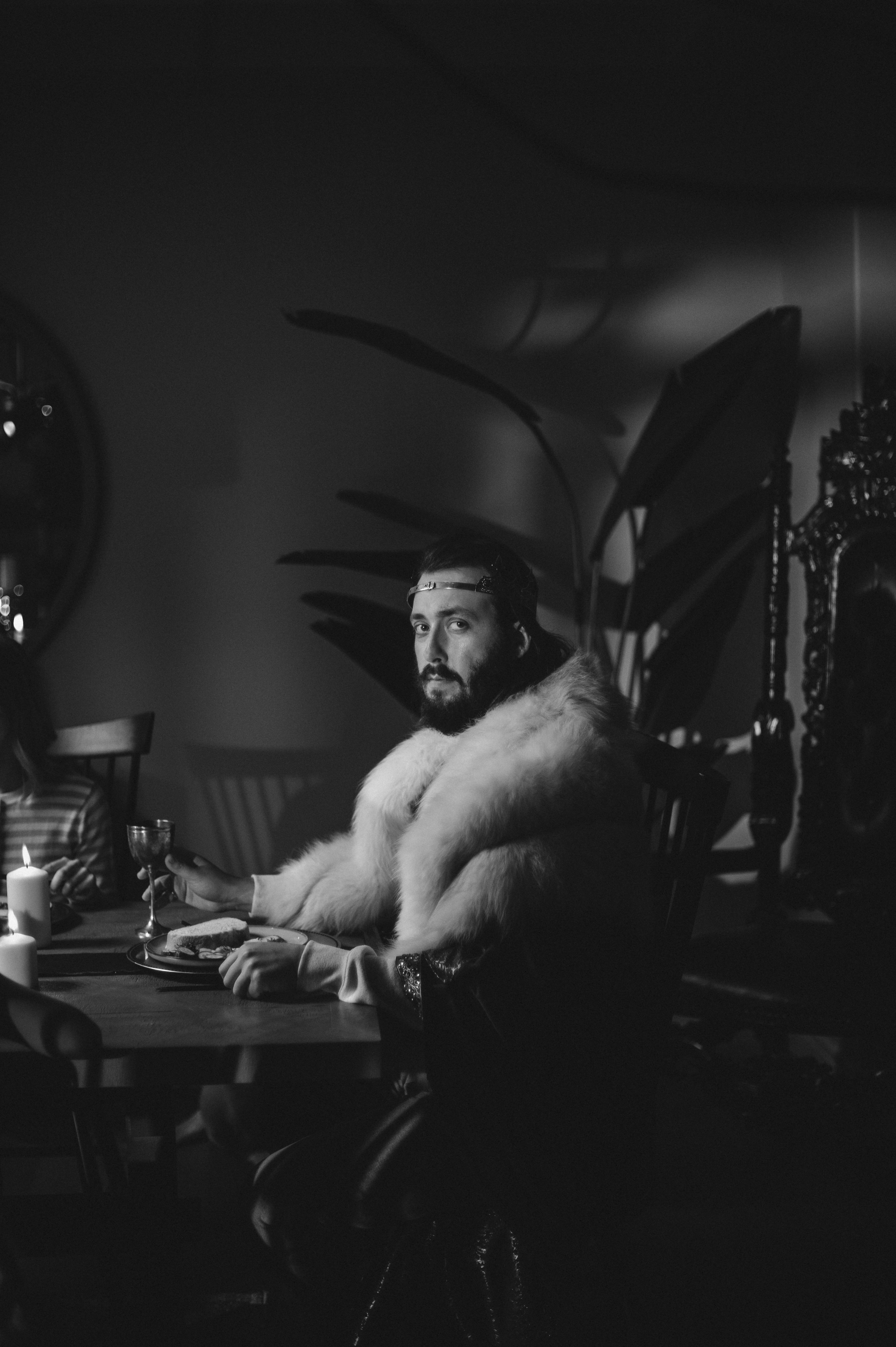 Homem de casaco de pele segurando copo de vinho à mesa.