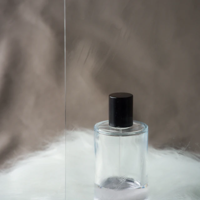 A clear glass perfume bottle with a black cap photographed against a plain background
