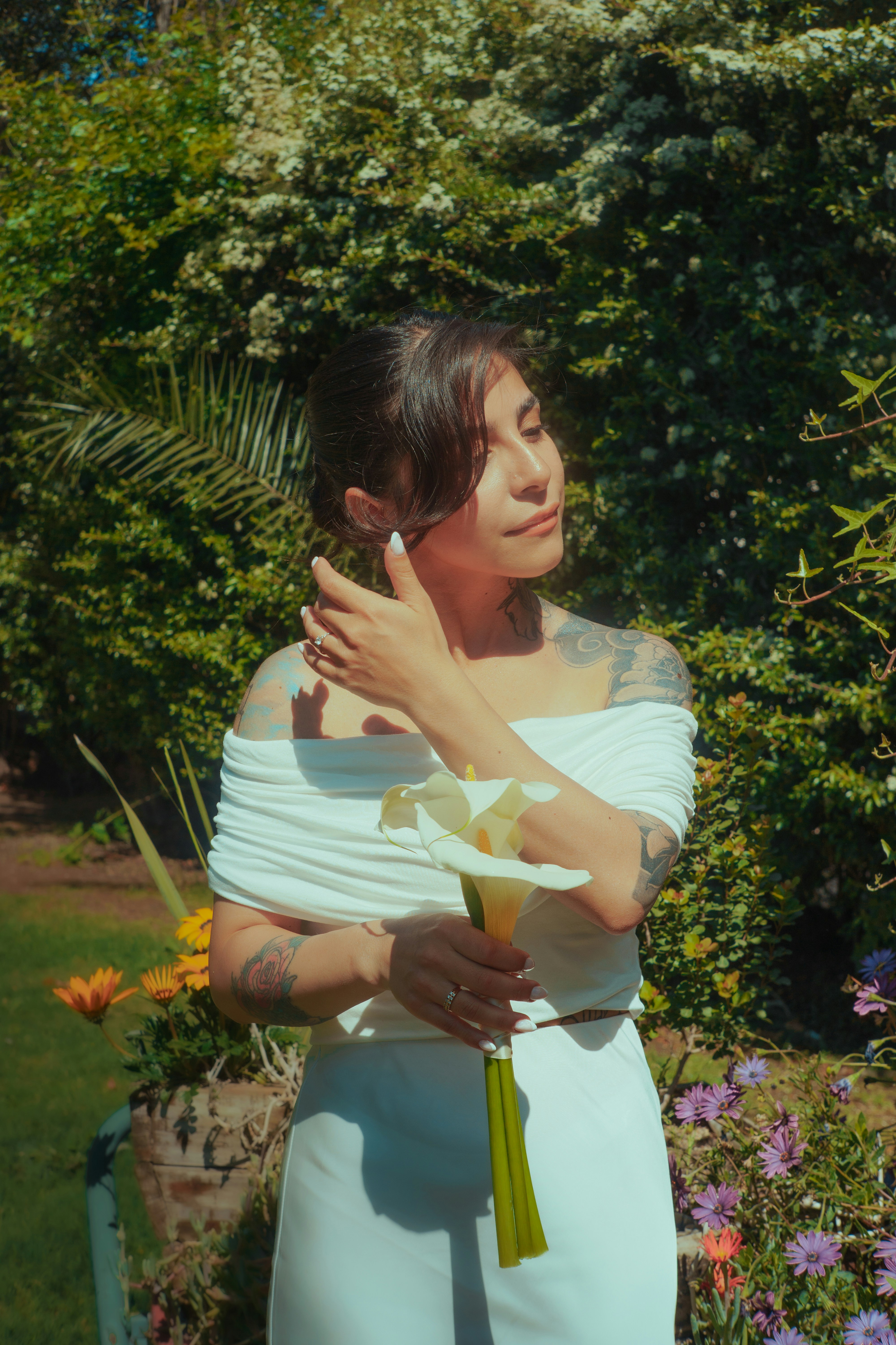Woman in white holding a calla lily in a garden.