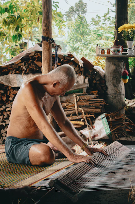 Elderly man weaving a mat indoors