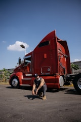 Man crouching in front of a red semi-truck.