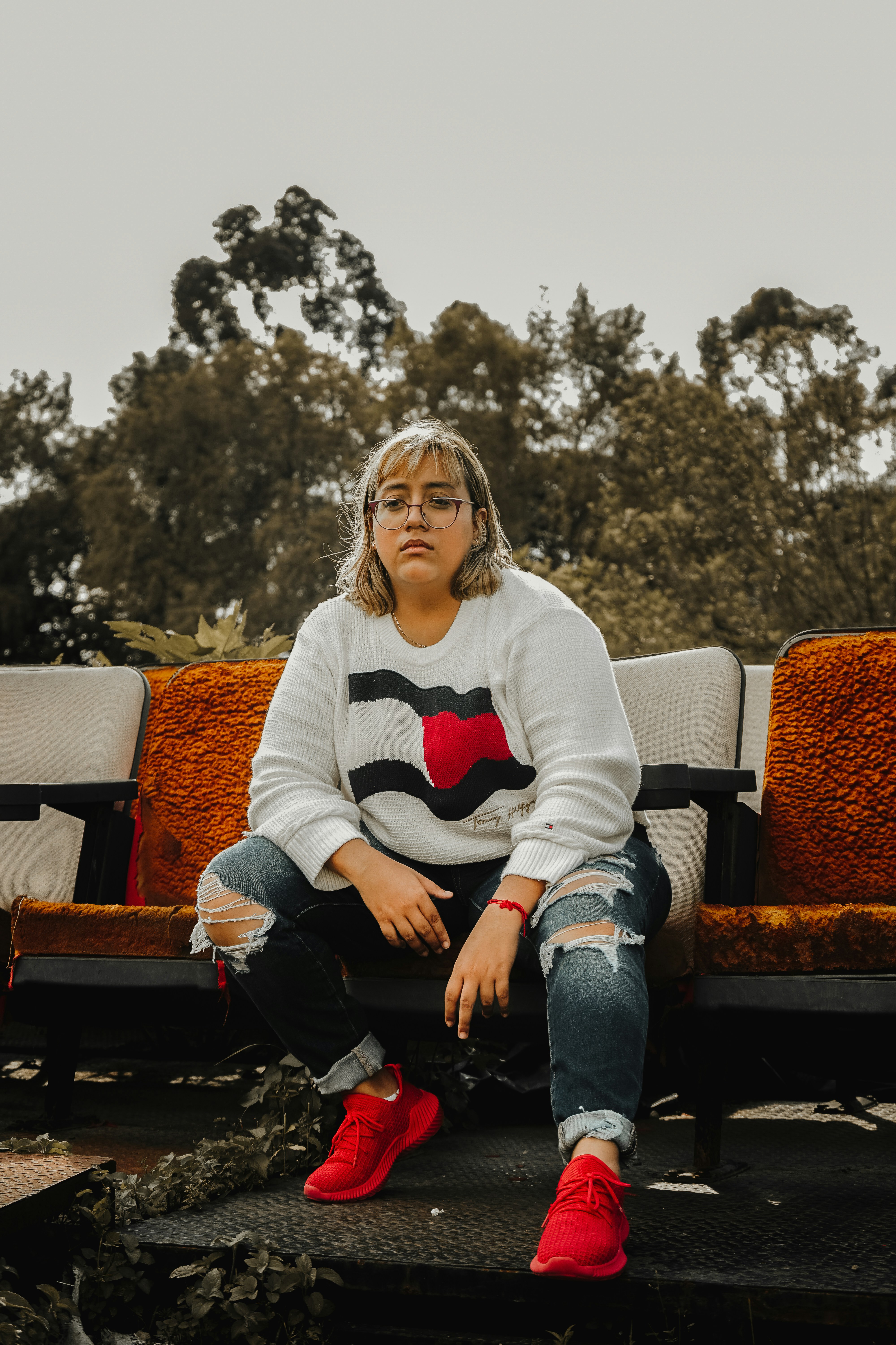 A woman in a sweater and ripped jeans sits outdoors.