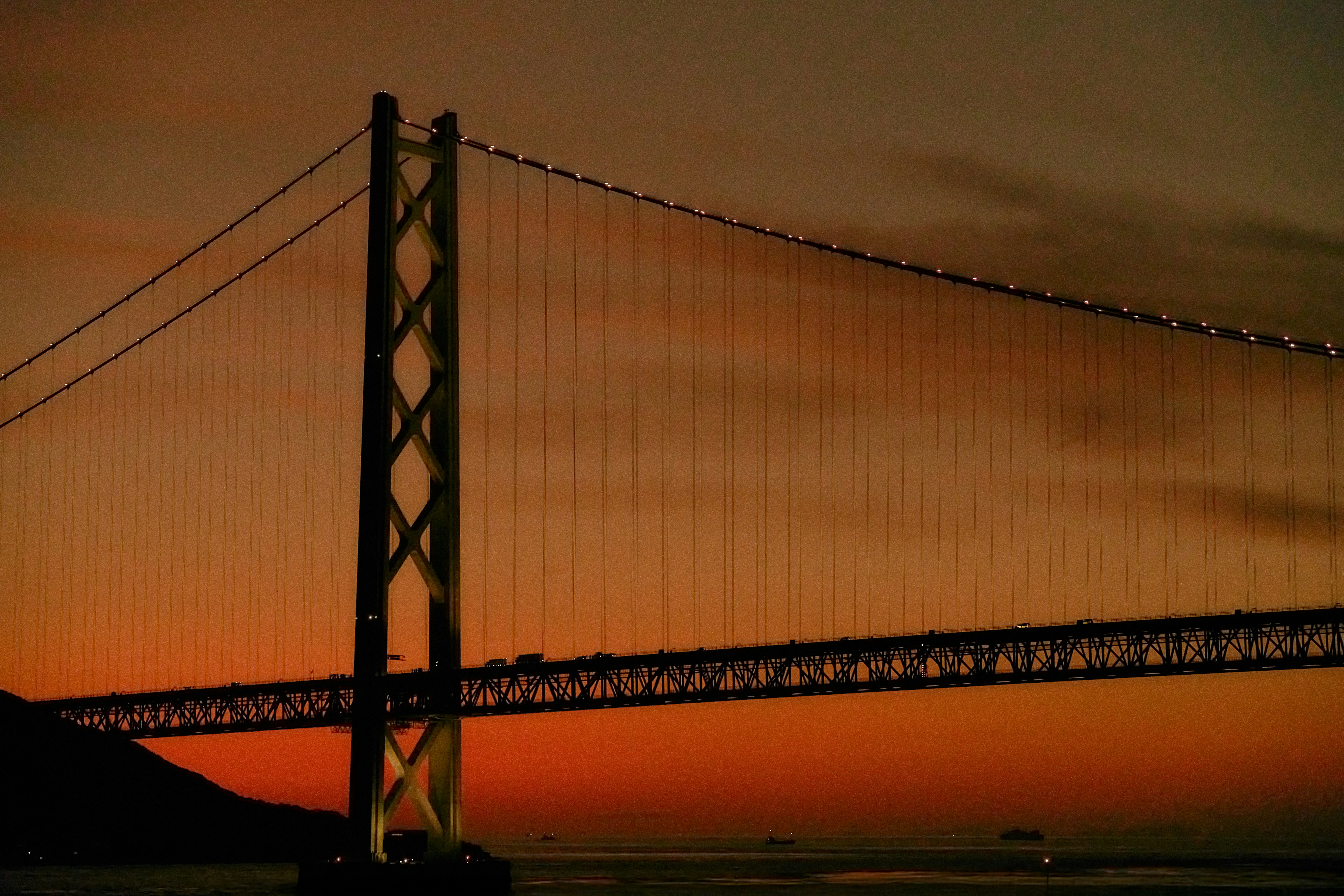Suspension bridge illuminated against a dramatic sunset sky.