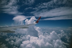 Airplane wing flying over fluffy white clouds