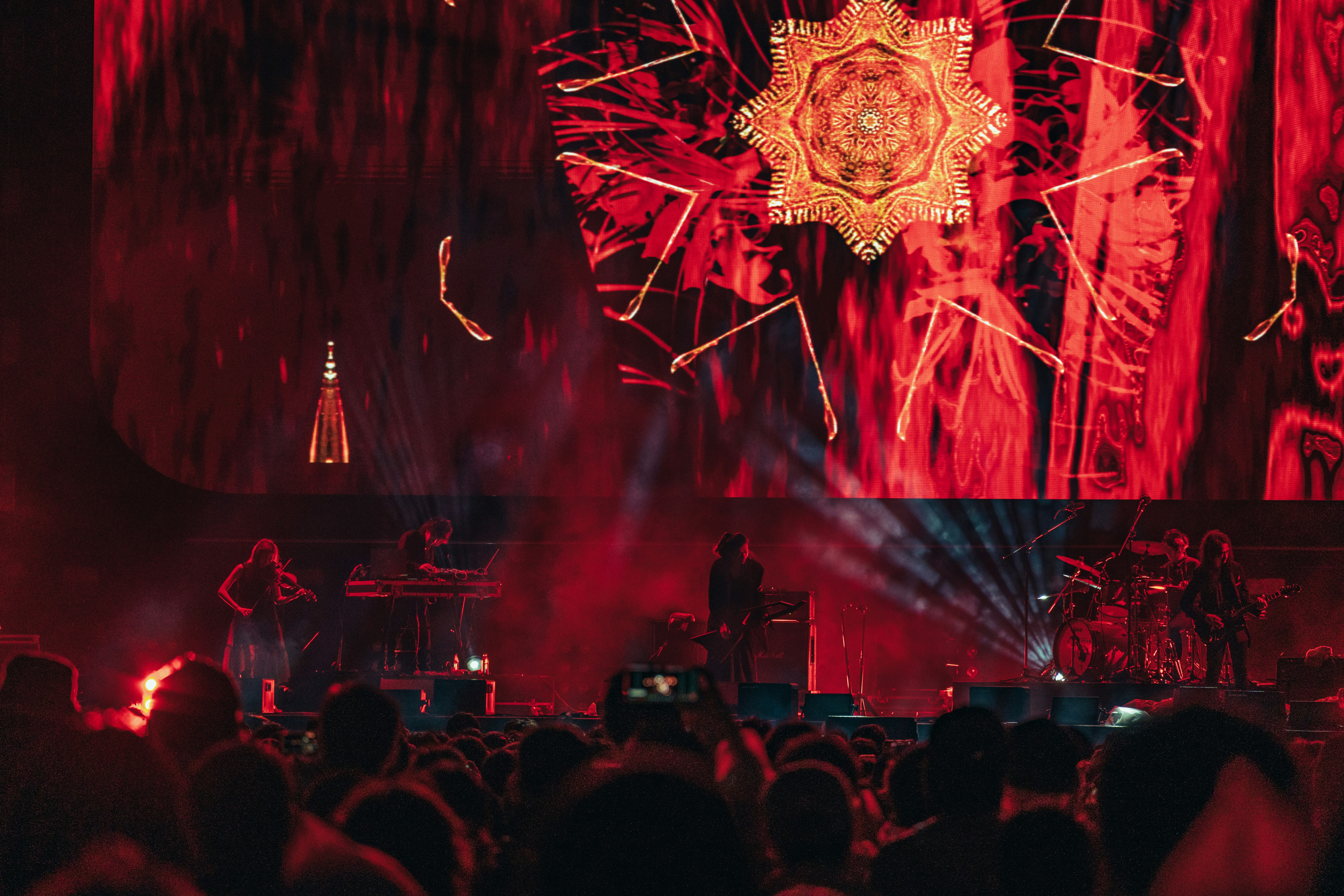 Band performing on stage with red lighting and gold visuals.