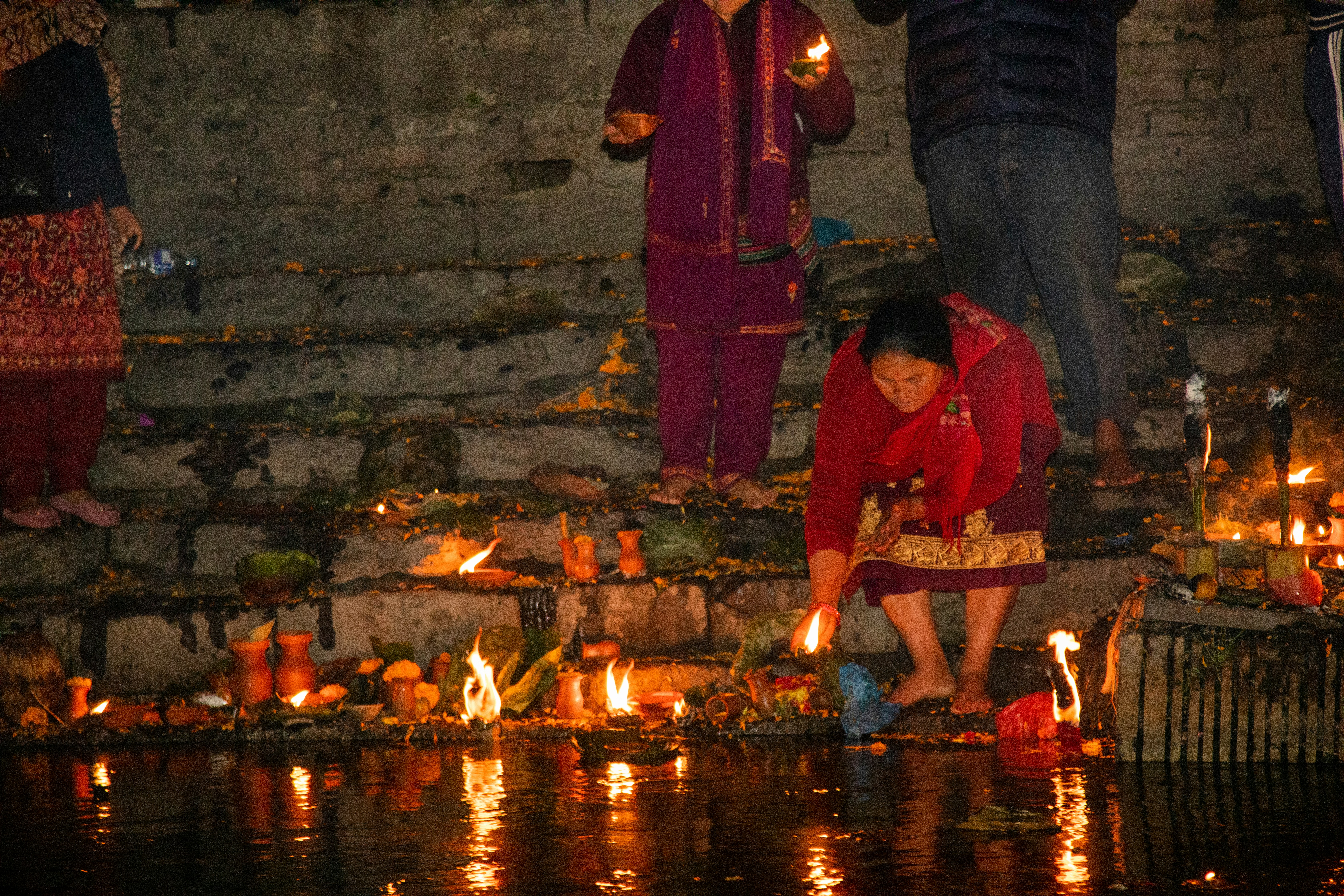 People gathered at a riverbank, lighting candles and offering flowers in memory of the victims, with worried faces in the crowd.
