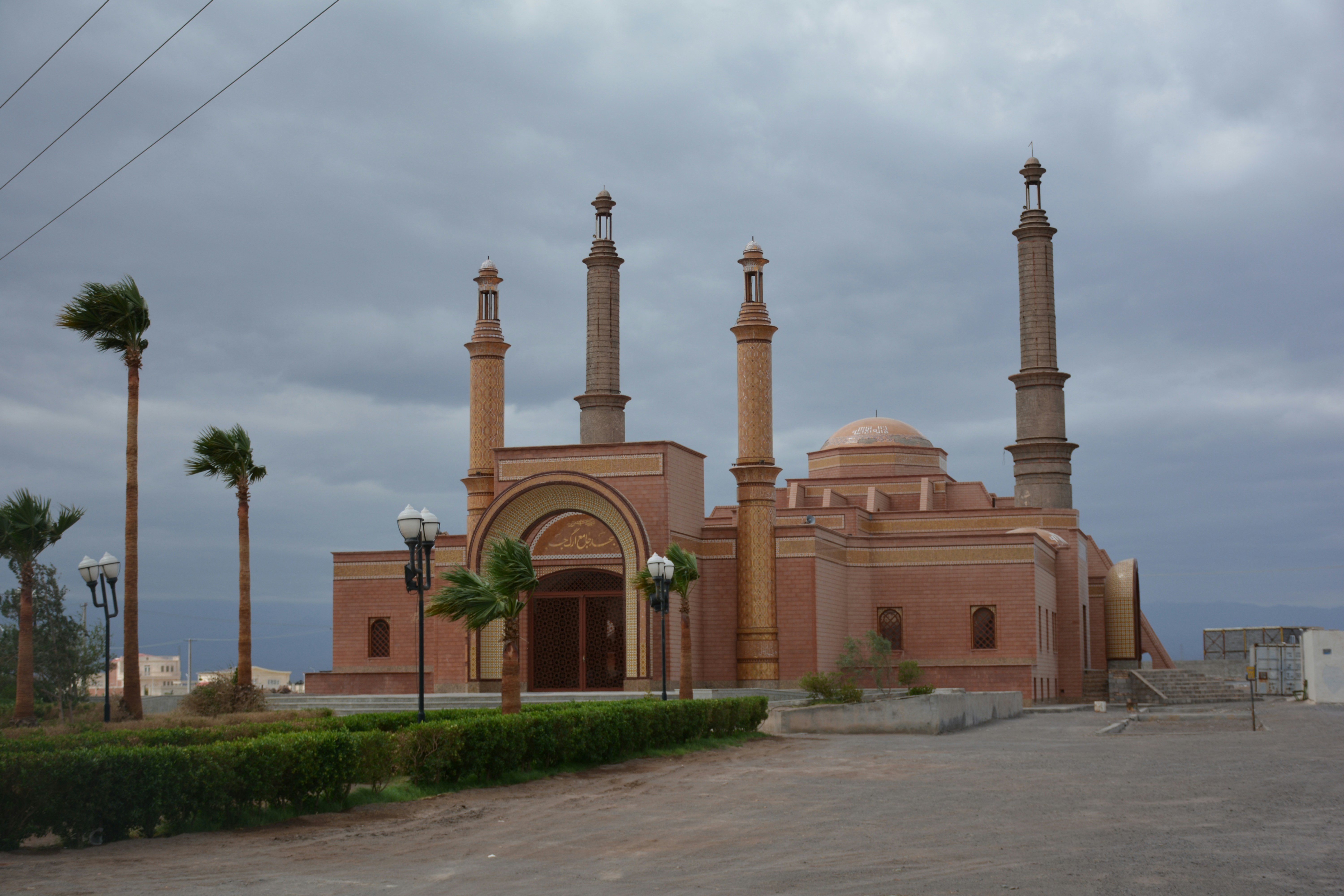 A mosque with minarets and palm trees under cloudy sky