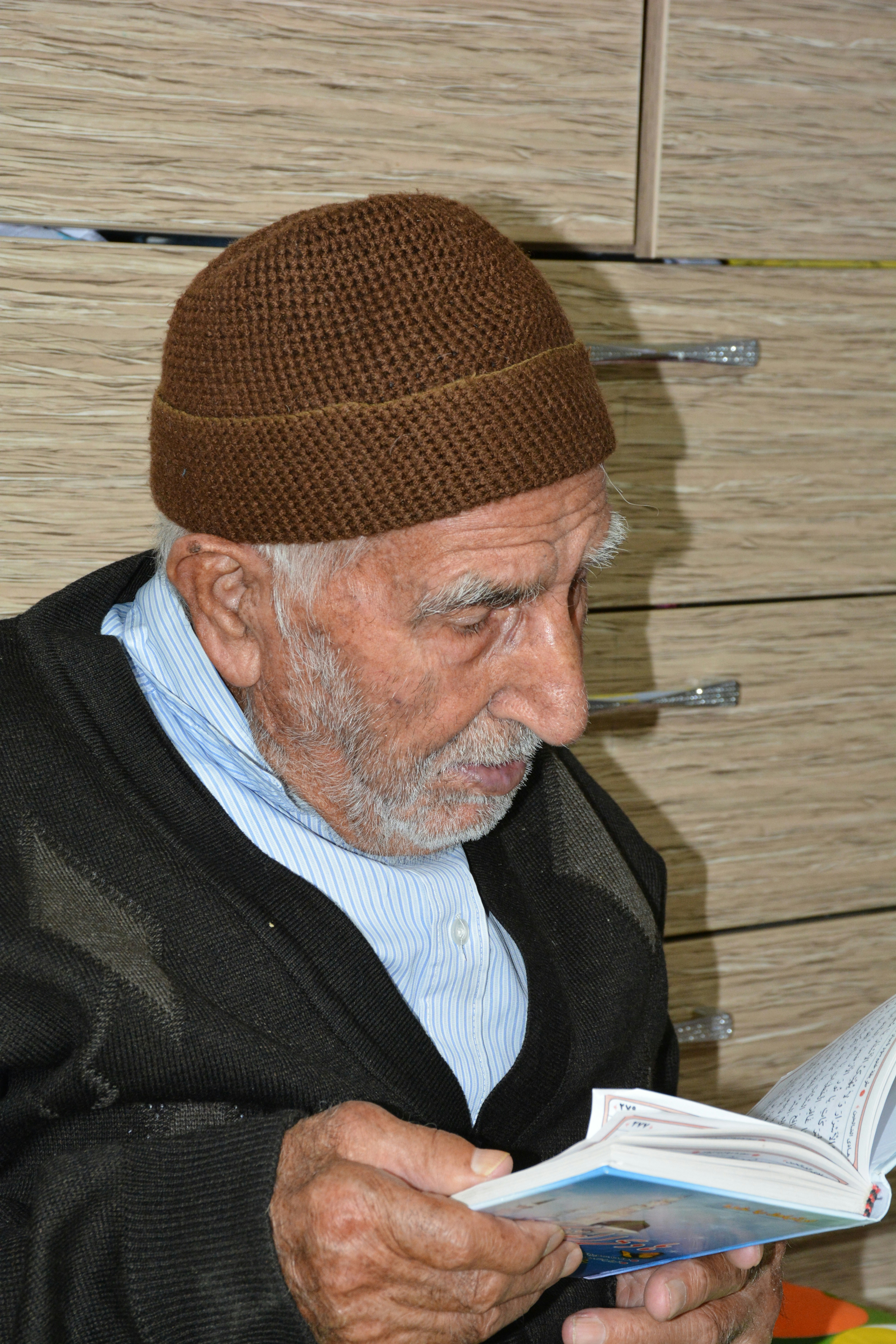 Elderly man wearing a brown knit cap reads a book