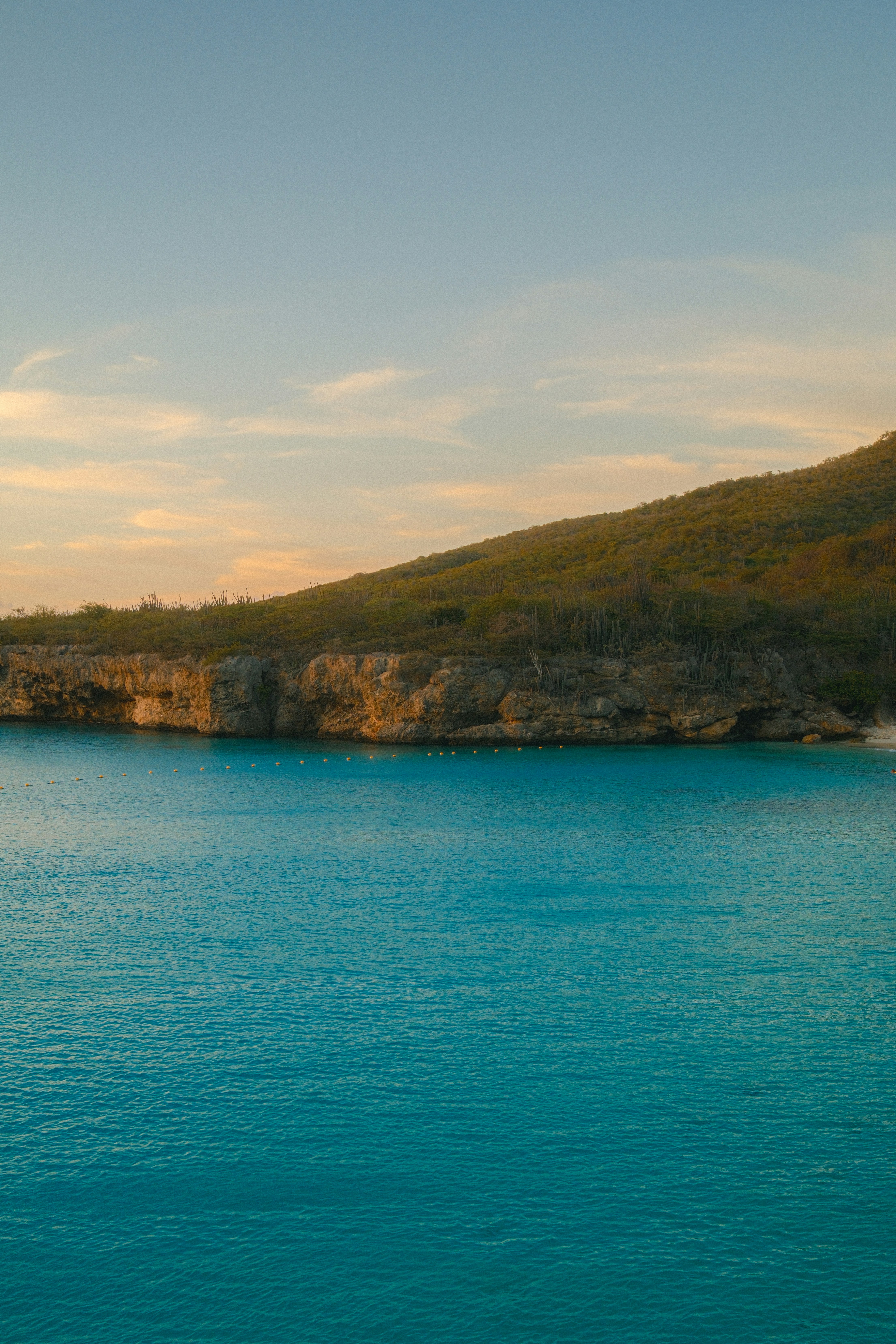L’eau turquoise rencontre un littoral rocheux et couvert d’arbres au coucher du soleil.