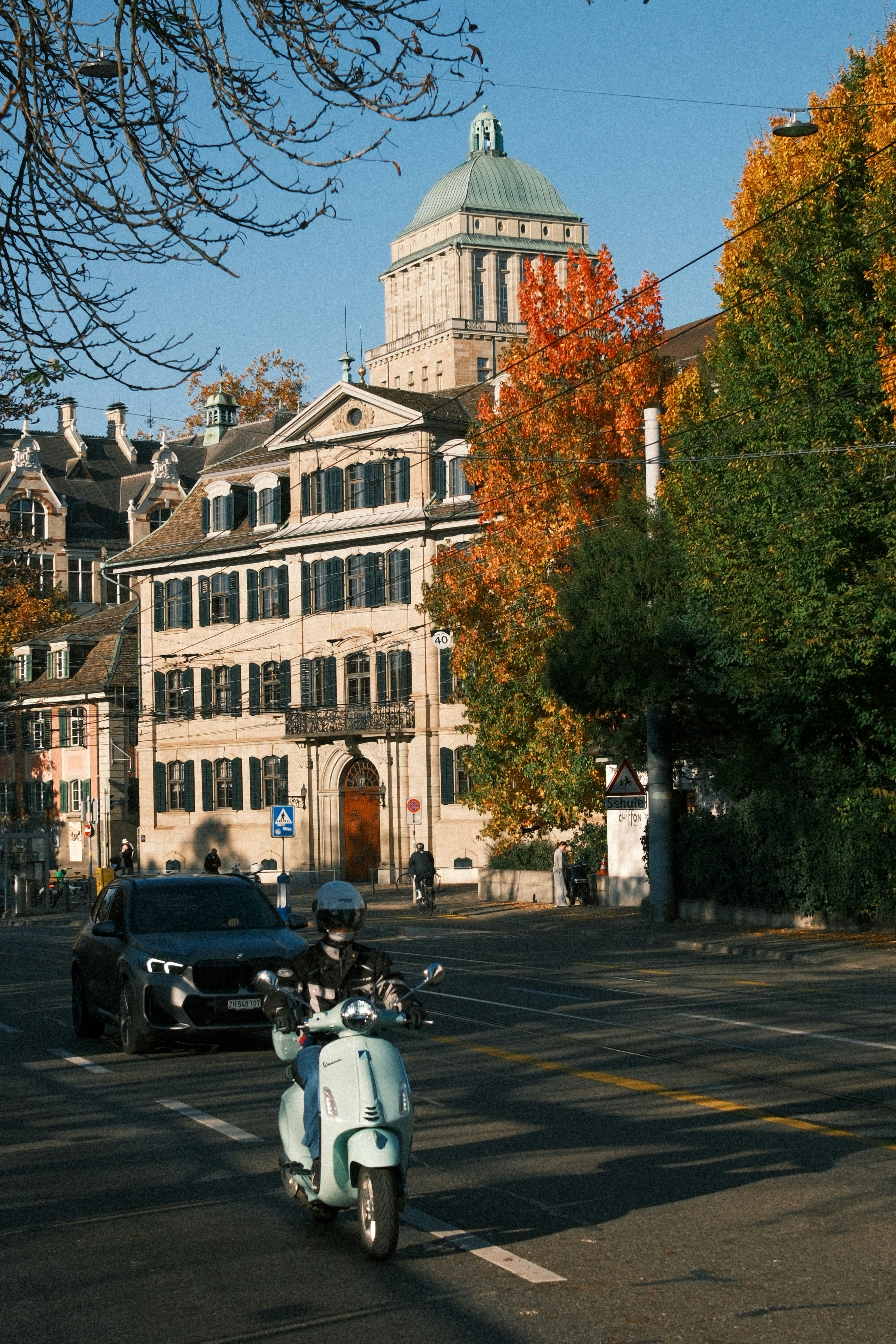 Scooter rider on street with autumn trees and building.