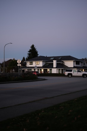 White truck drives past houses at dusk