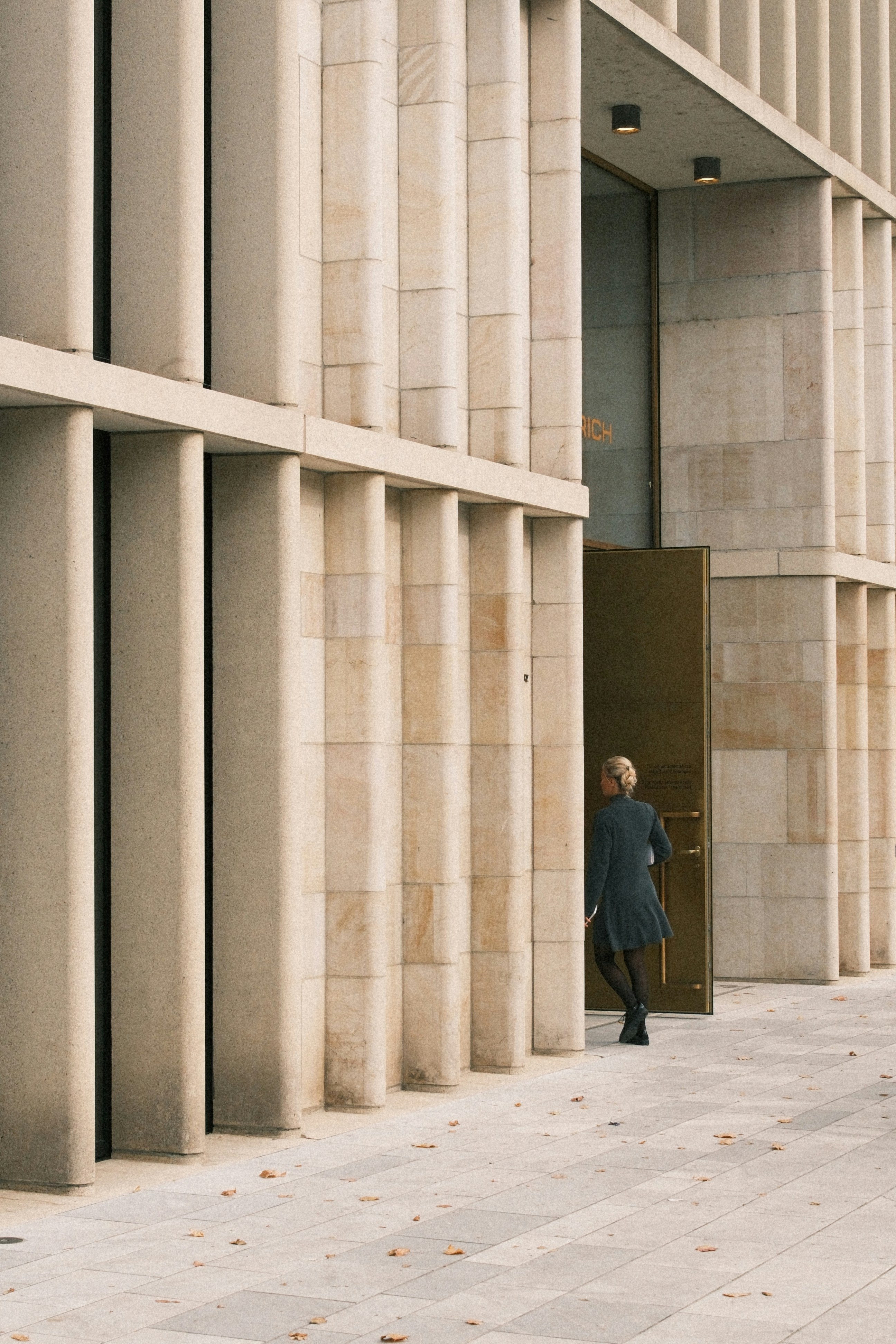 Woman entering a modern building with stone facade.