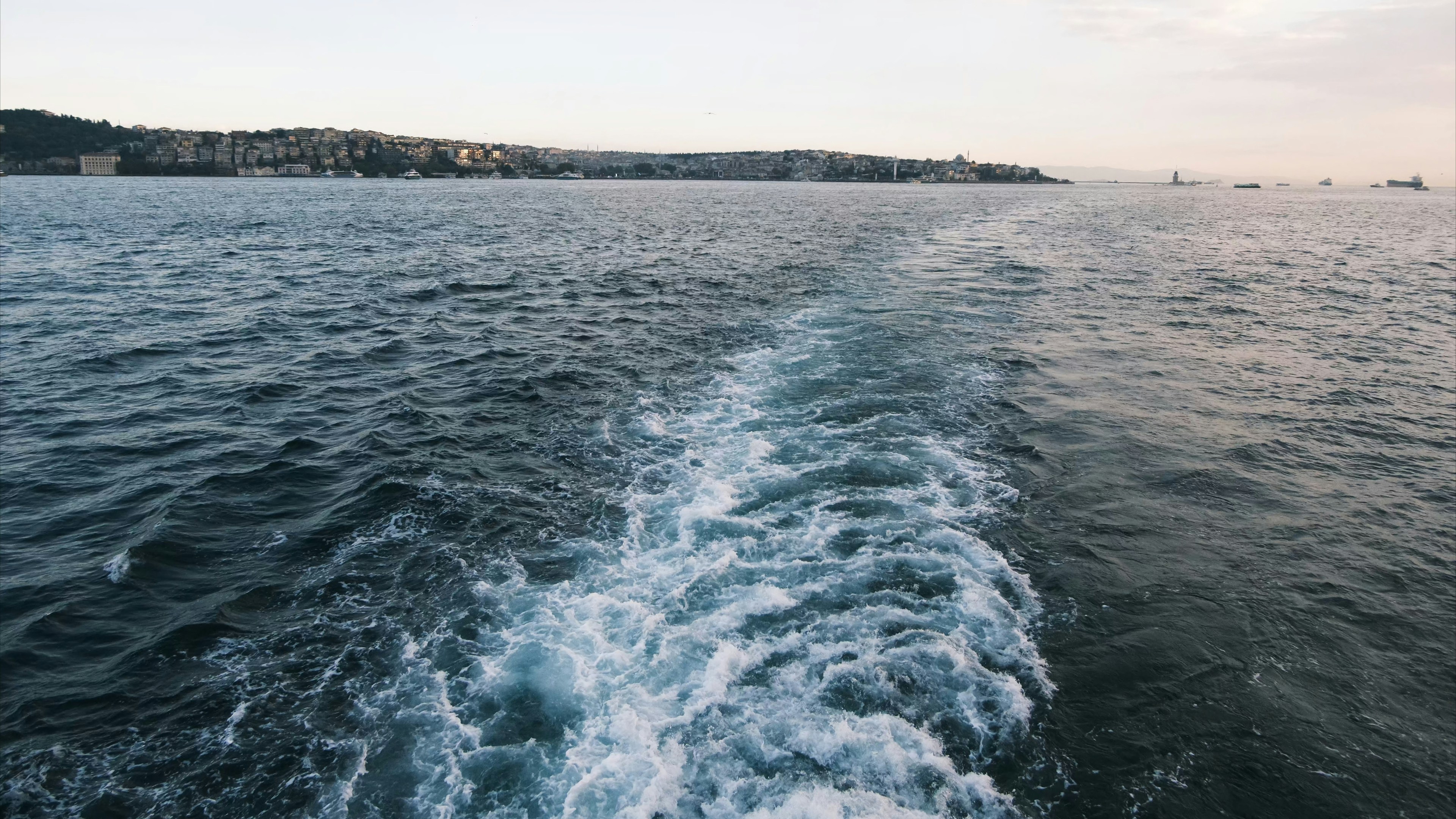Wake of a boat on the ocean near city (Photo by Cemrecan Yurtman on Unsplash)