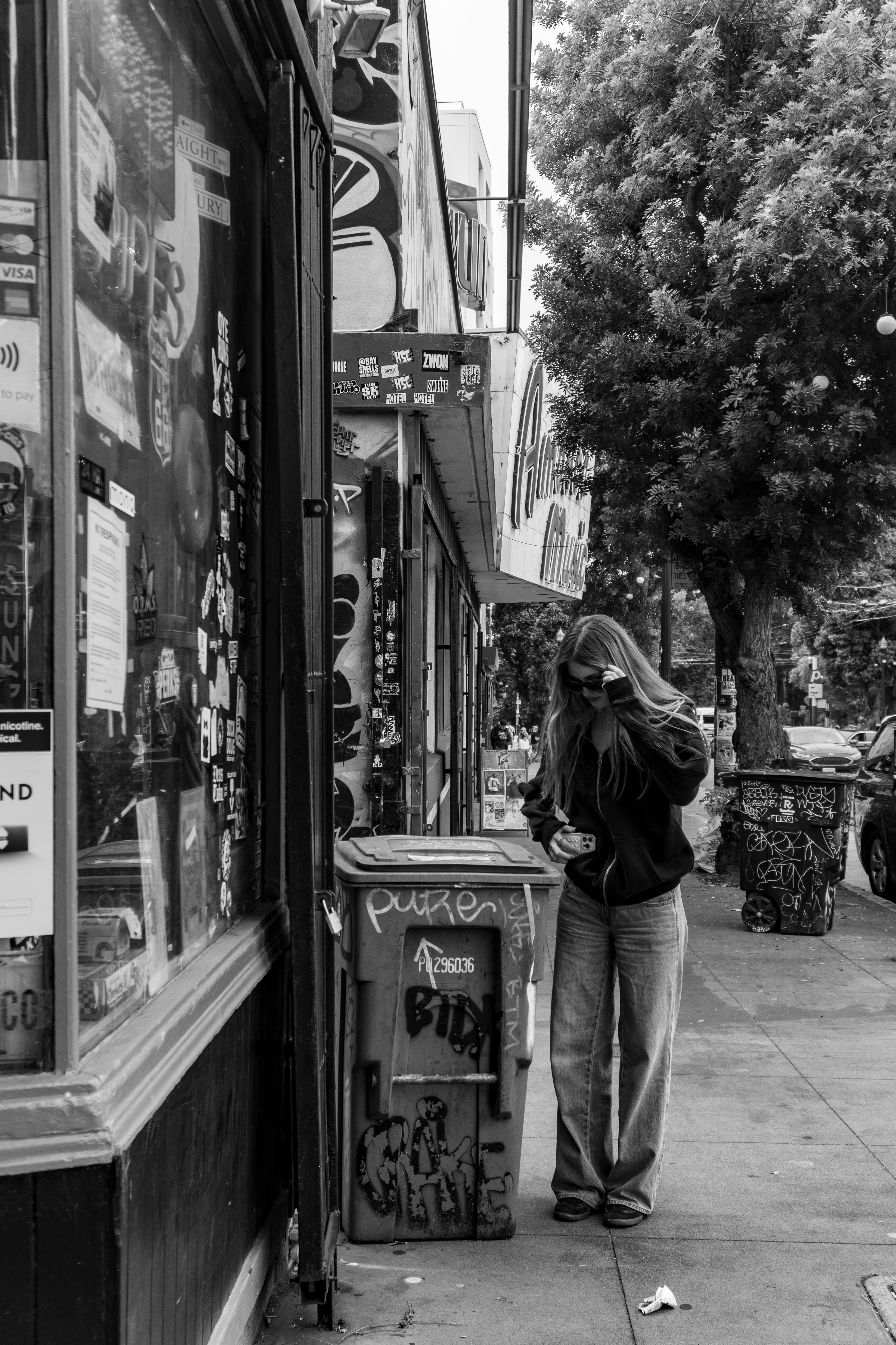 Mujer parada en la acera junto a un bote de basura.