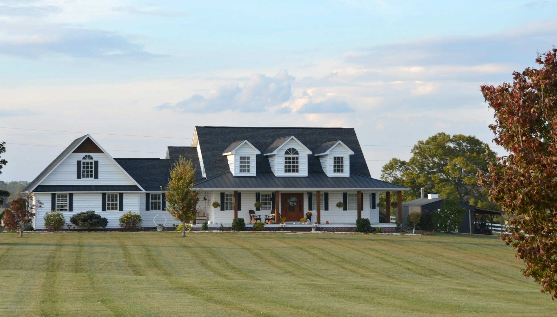 A large white farmhouse with a wrap-around porch.