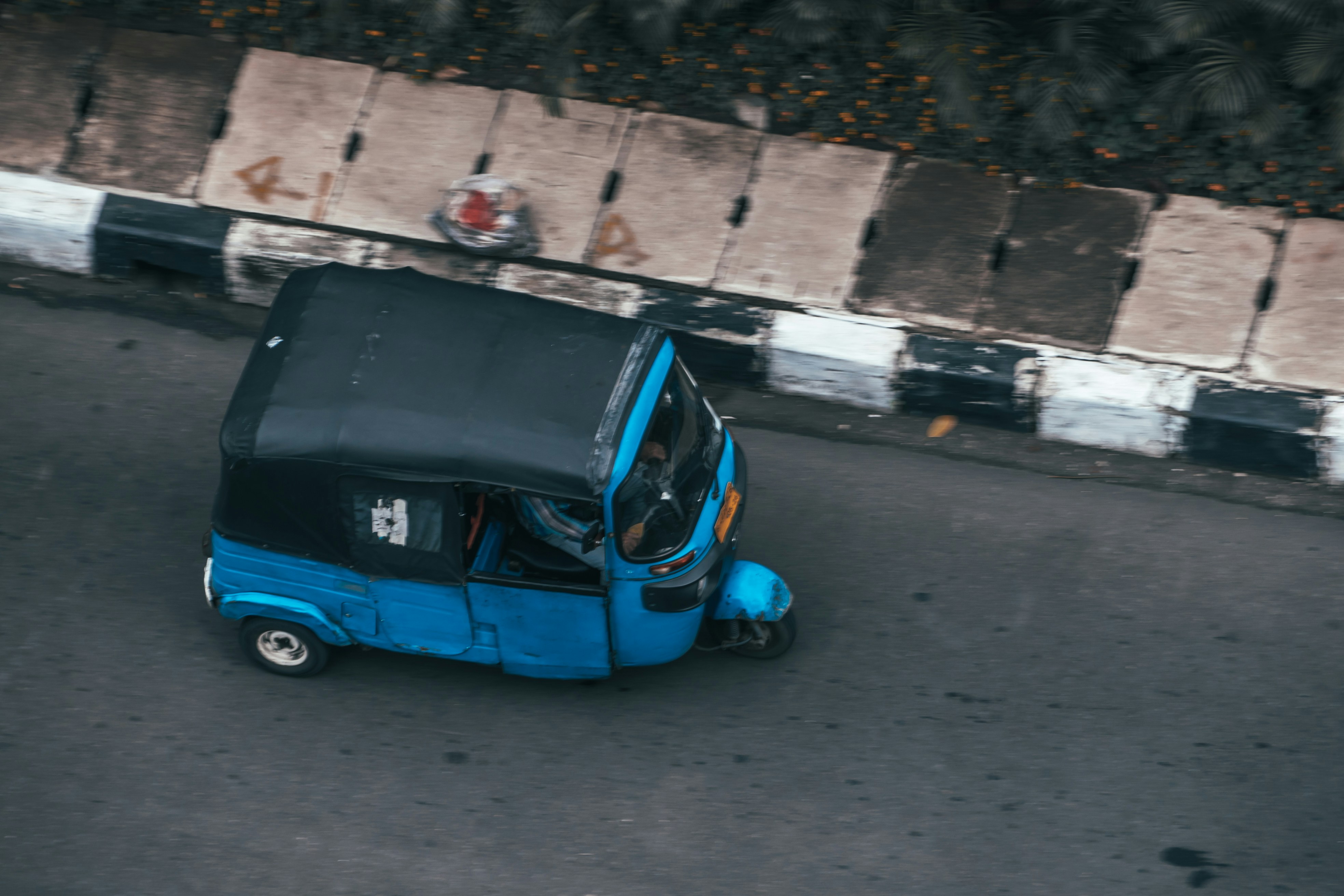 A blue auto-rickshaw drives on a street.