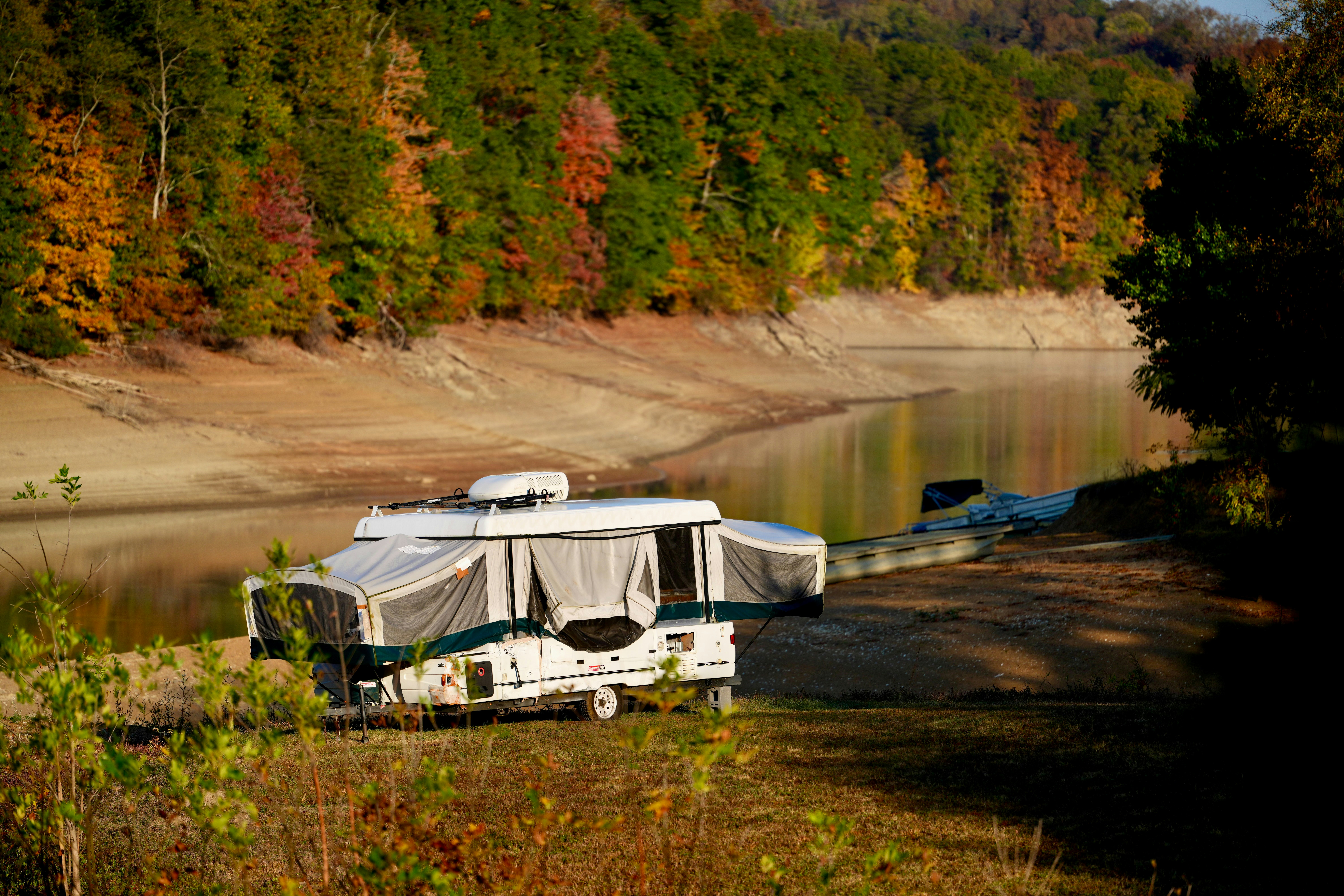 Pop-up camper parked by a calm lake in autumn.