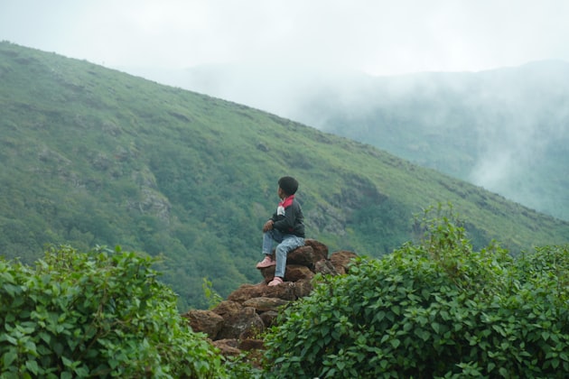 Personne assise sur des rochers face à des montagnes brumeuses