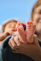 Tiny baby feet covered in sand held by parent