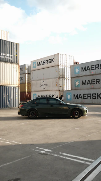 Dark sedan parked near stacked shipping containers