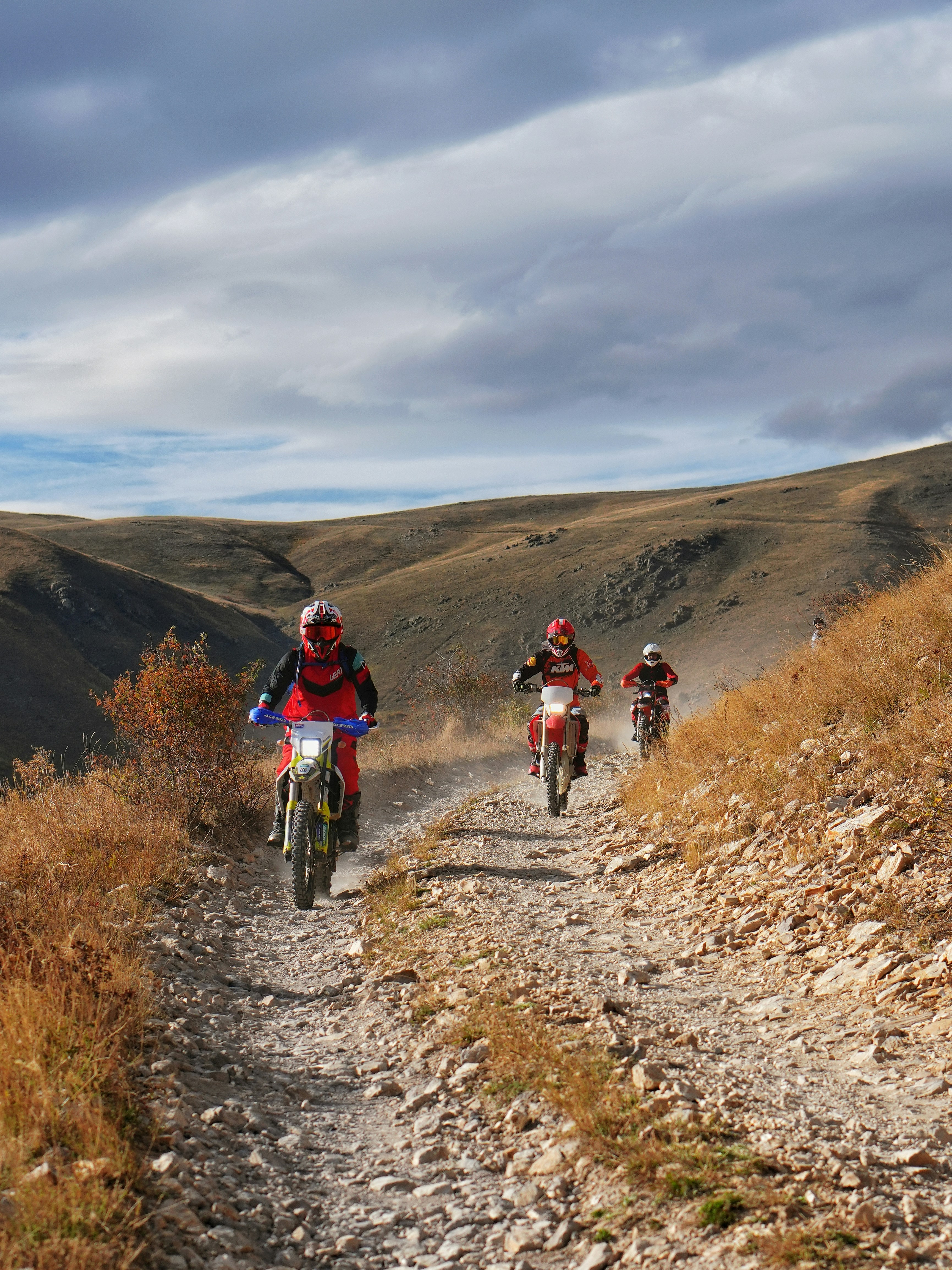 Three motorcyclists ride down a rocky mountain trail.