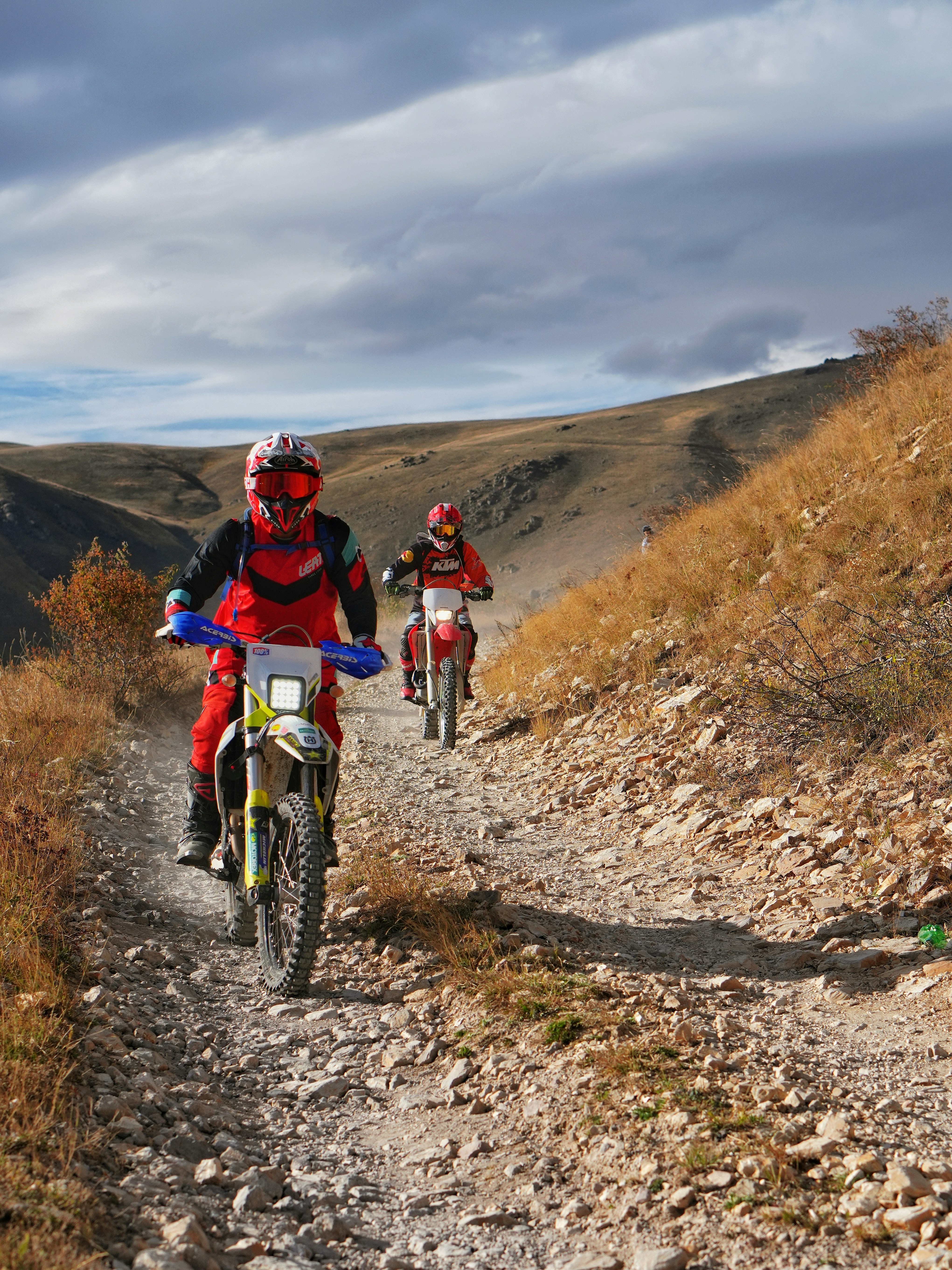 Two motorcyclists ride on a rocky mountain trail.