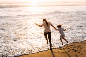 Mother and child running on beach at sunset