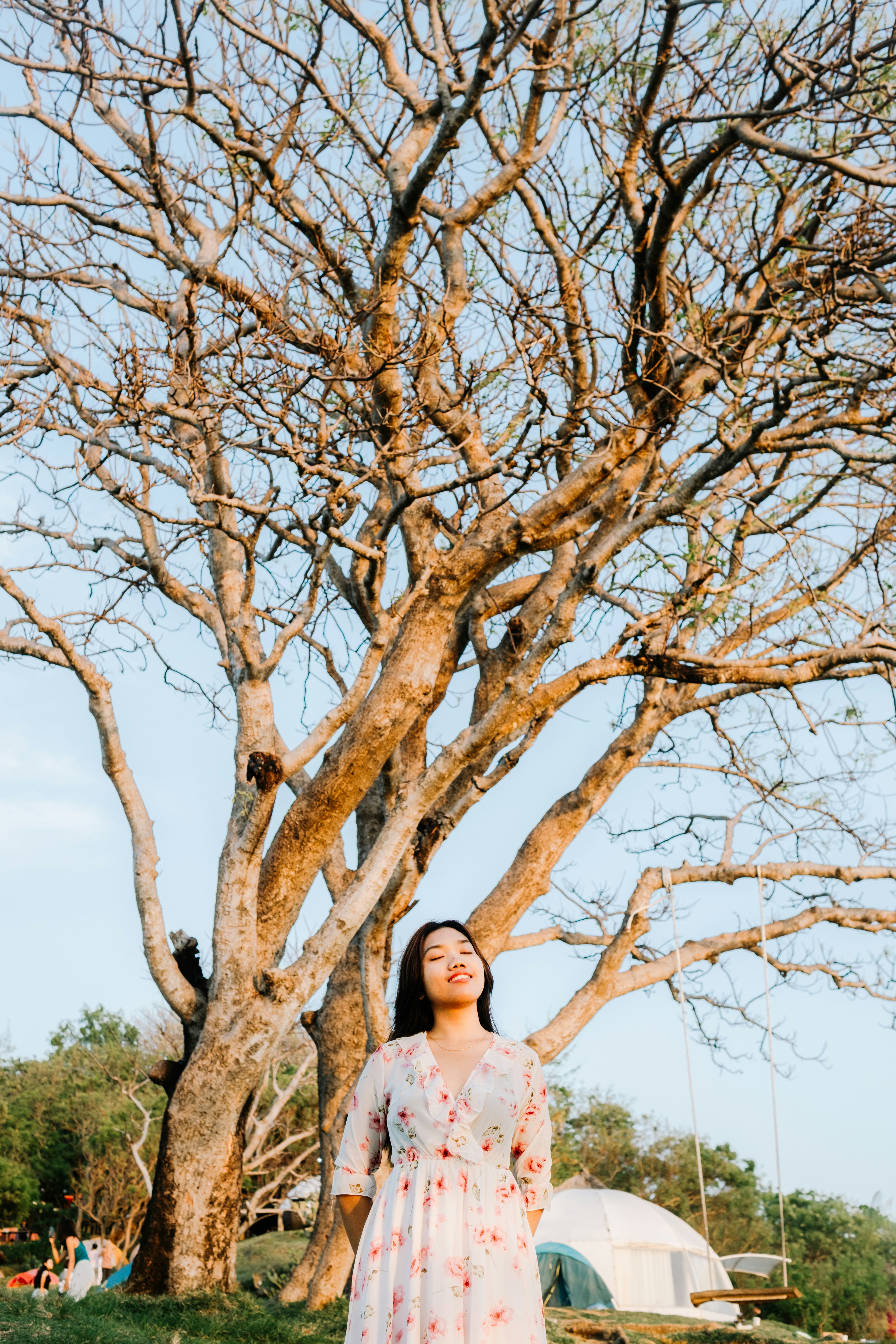 Woman in floral dress stands under large tree