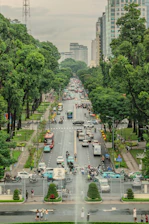 Busy city street with cars and trees under cloudy sky