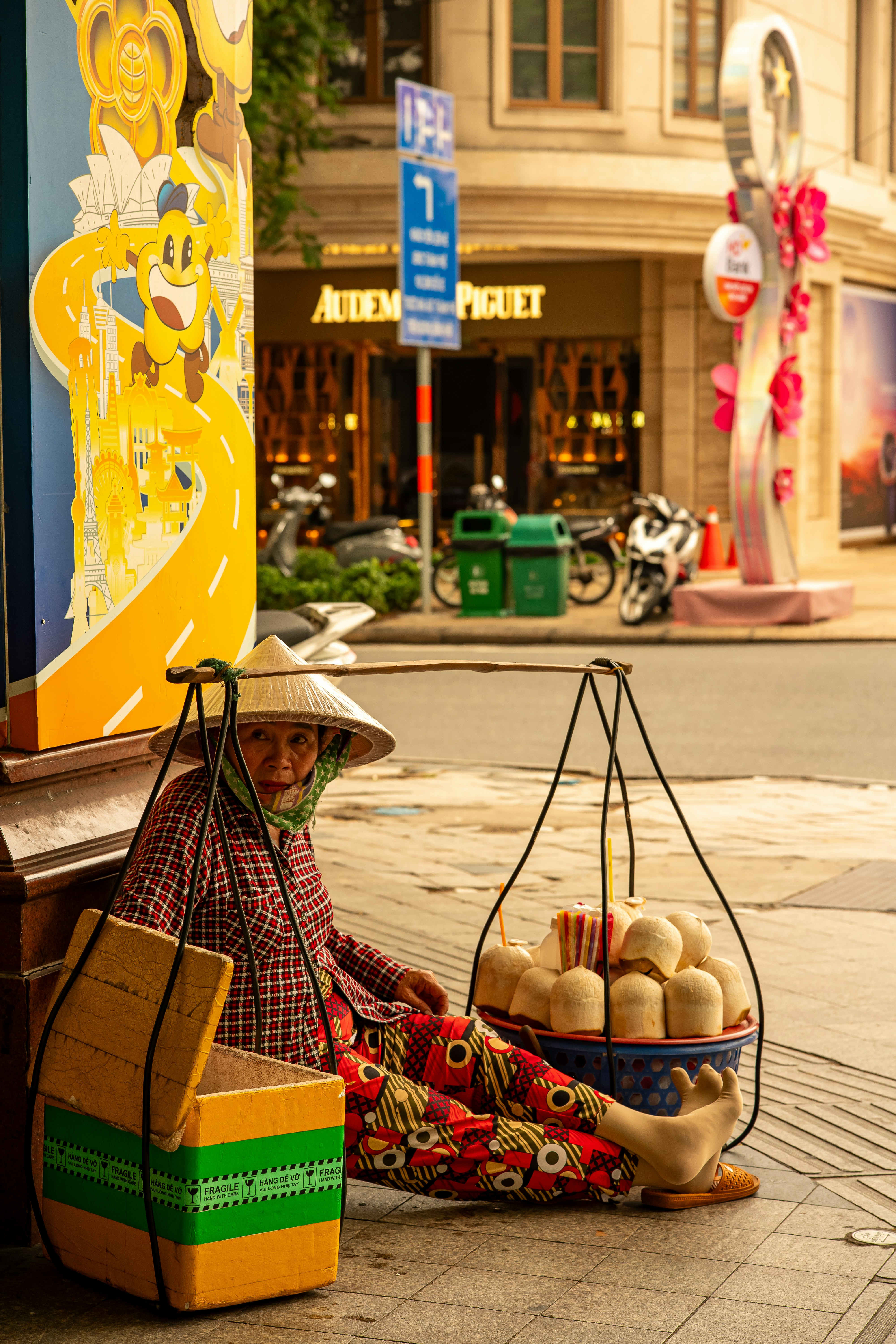 Woman in conical hat sells goods on a street.
