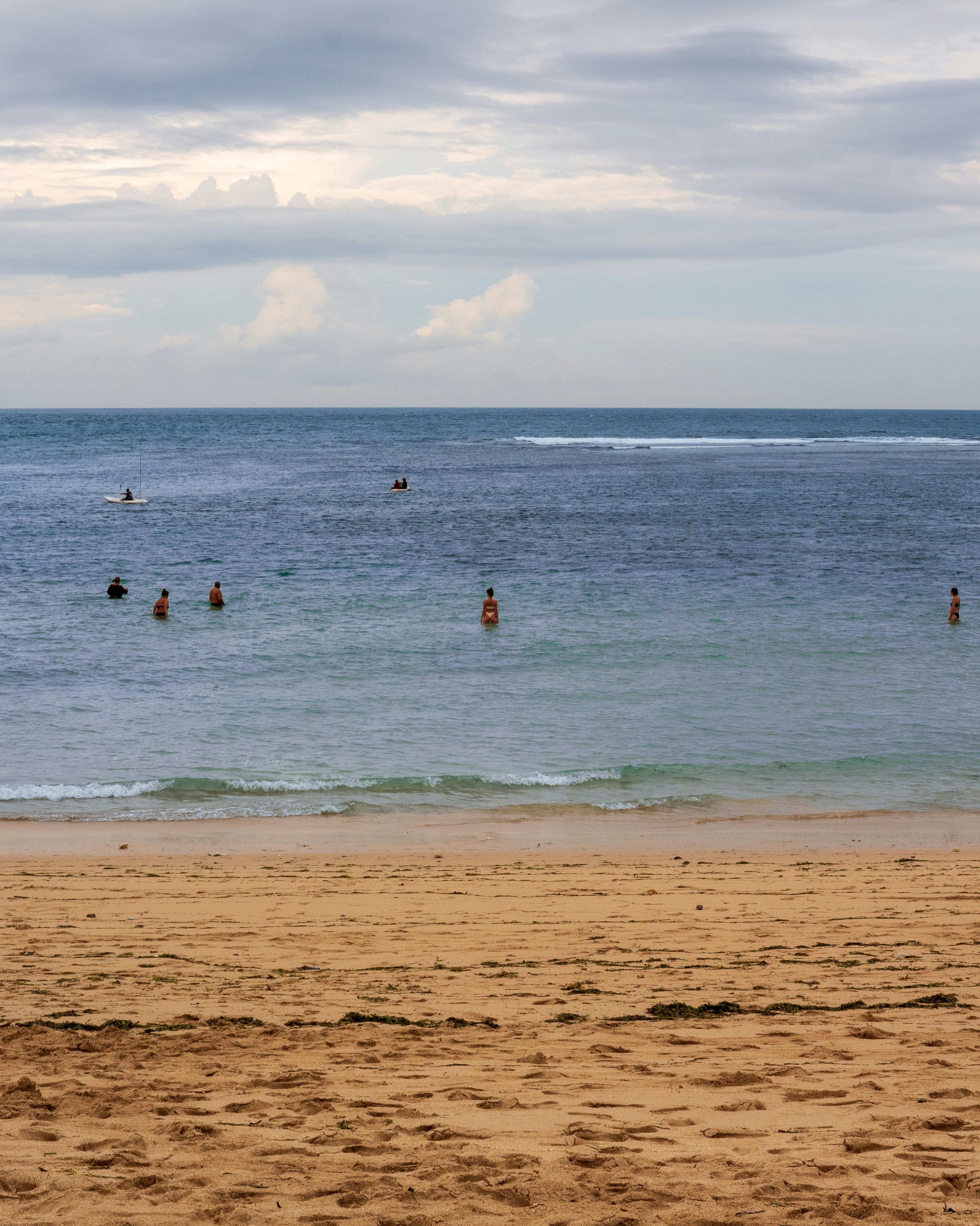 People swimming in the ocean near a sandy beach.