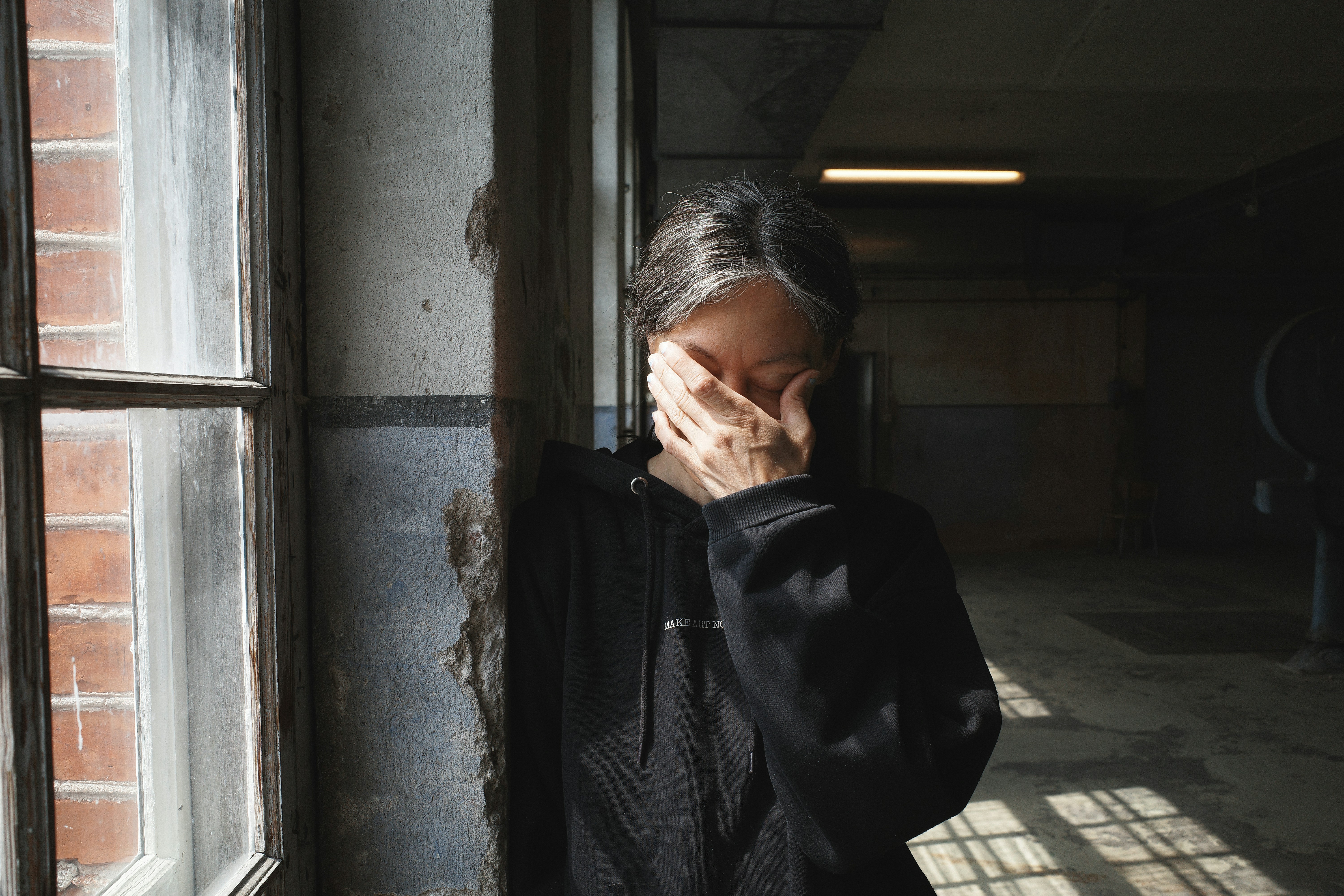 Person covers face with hand near window.